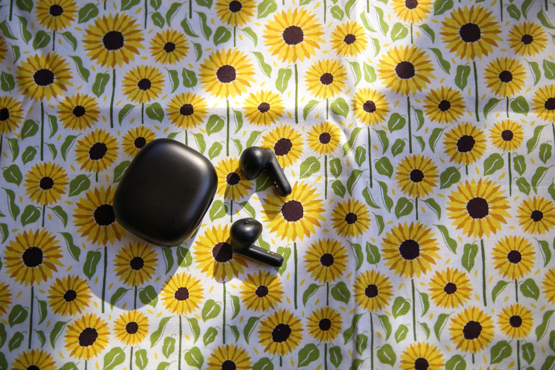 Photo of a set of black AirPods on a tablecloth with a sunflower pattern