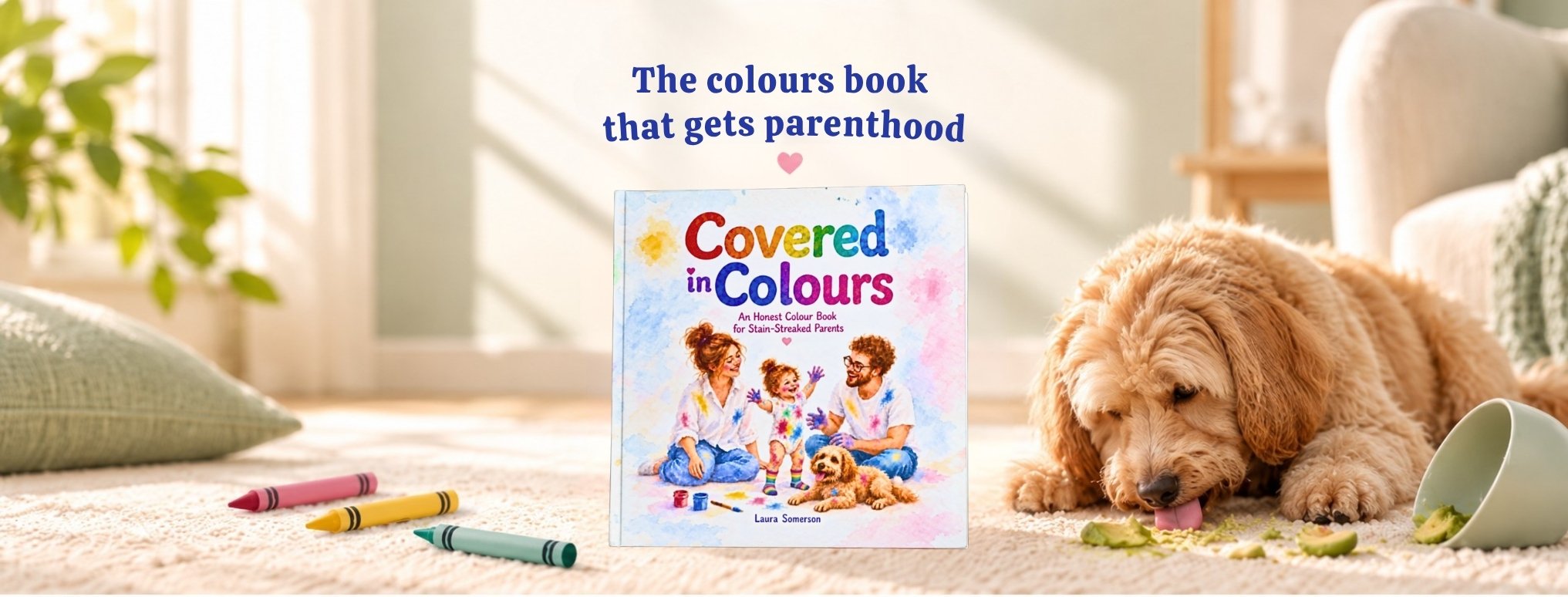 Covered in Colours children's picture book displayed in a sunlit living room, surrounded by colourful crayons and a fluffy dog. A heartwarming, relatable colours book celebrating the messy, colourful joy of parenthood, by Laura Somerson.