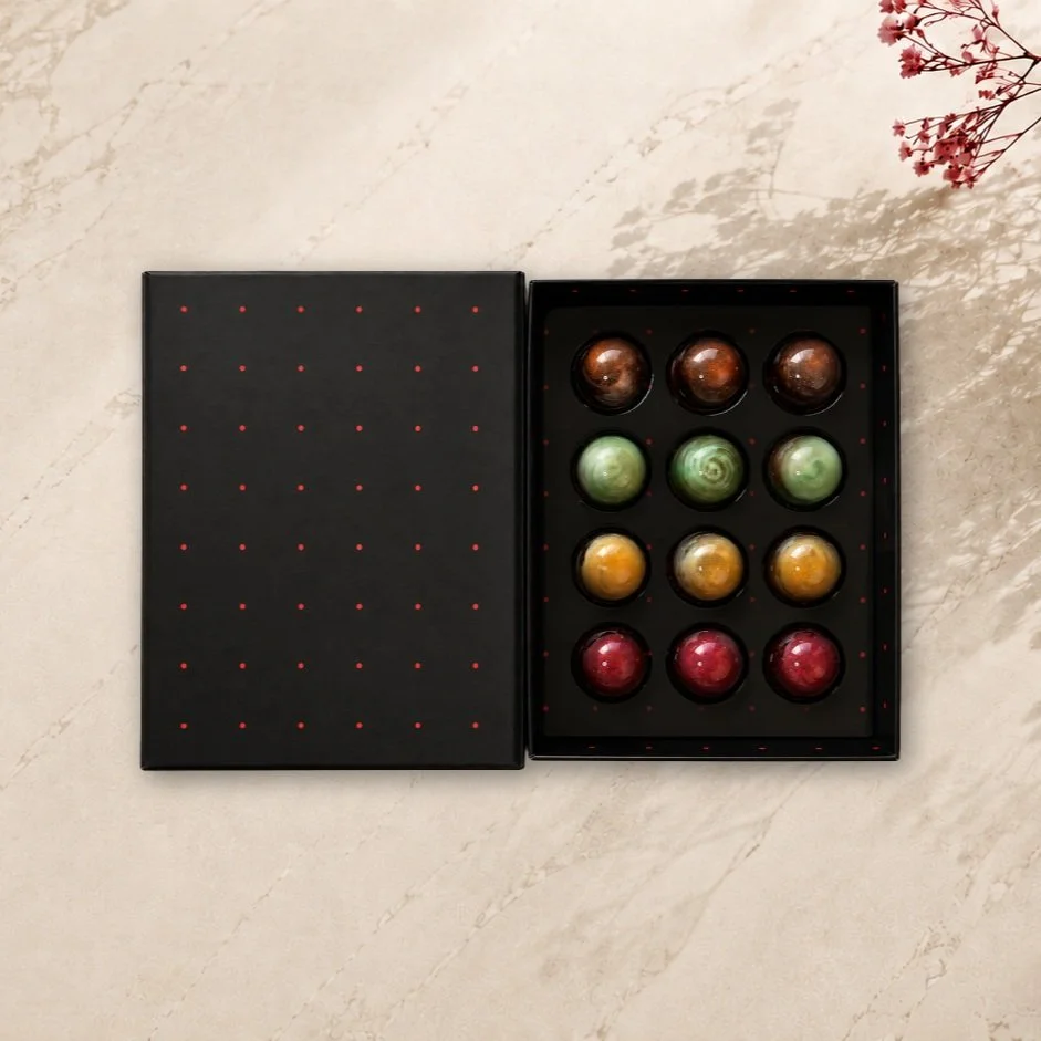 Our black Bonbon Library Box, filled with 12 handcrafted bonbons inspired by 4 classic drinks:

Bourbon Caramel
Muscat
Mojito
Espresso Martini 

Rich, grown-up, a little bit boozy.
Local delivery is available this Father's Day for the first time &mda