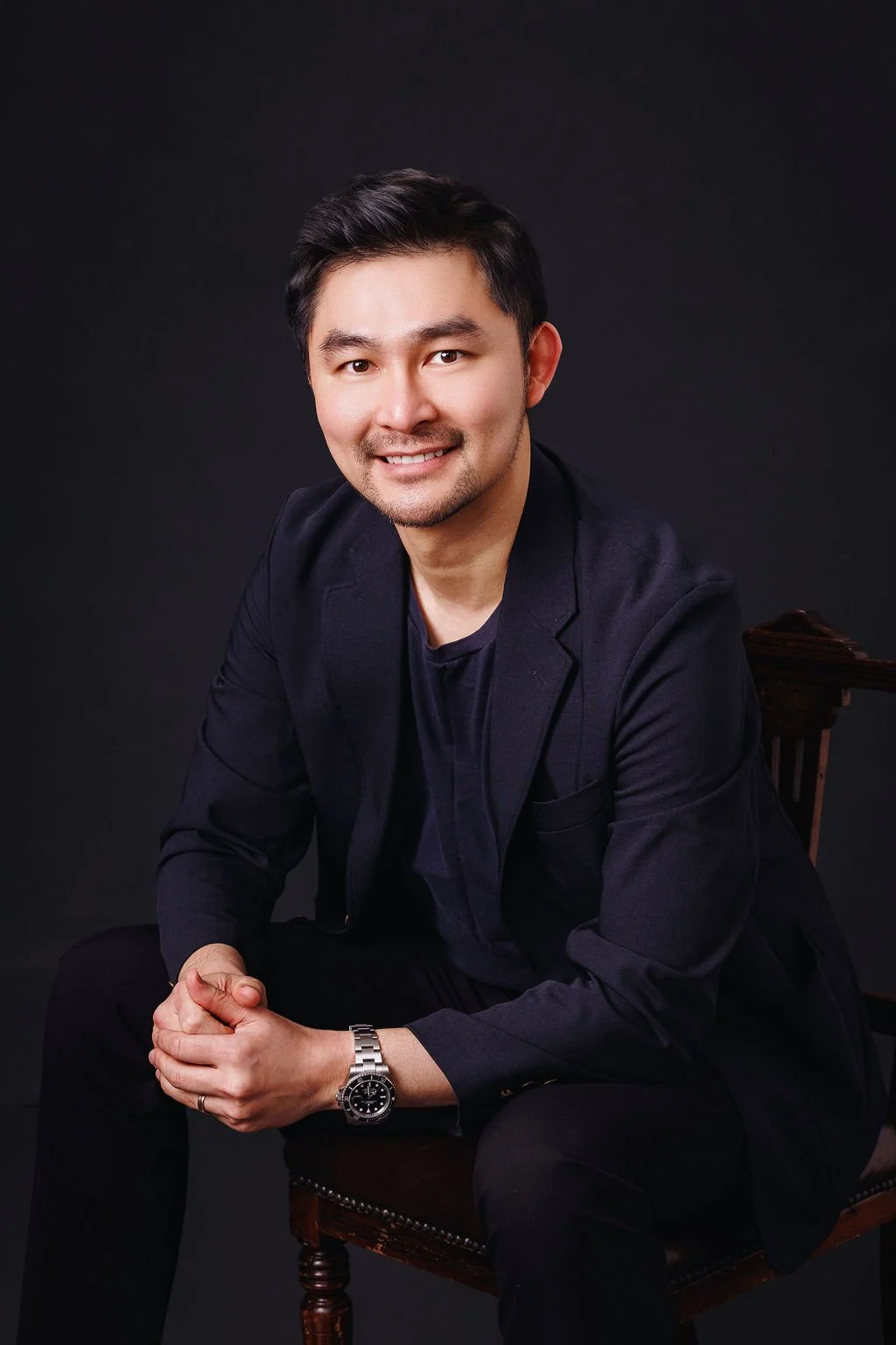 A smiling man with short black hair, wearing a dark blazer and light shirt, against a white background.