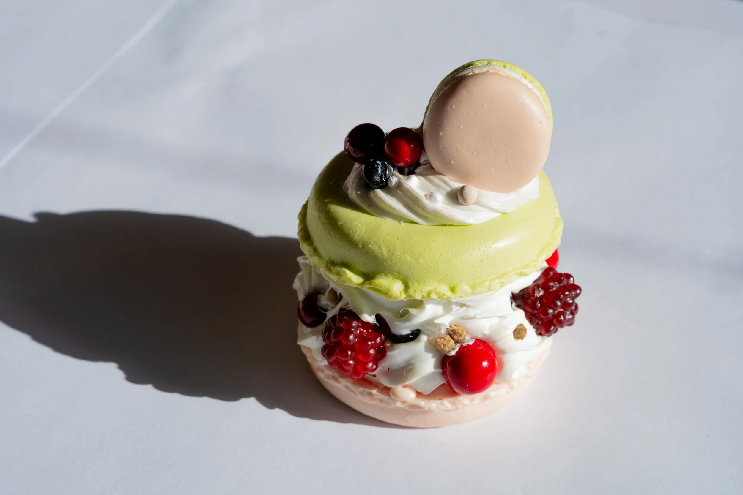 A colorful layered dessert with cream, berries, and a pink macaron on top, placed on a white surface.