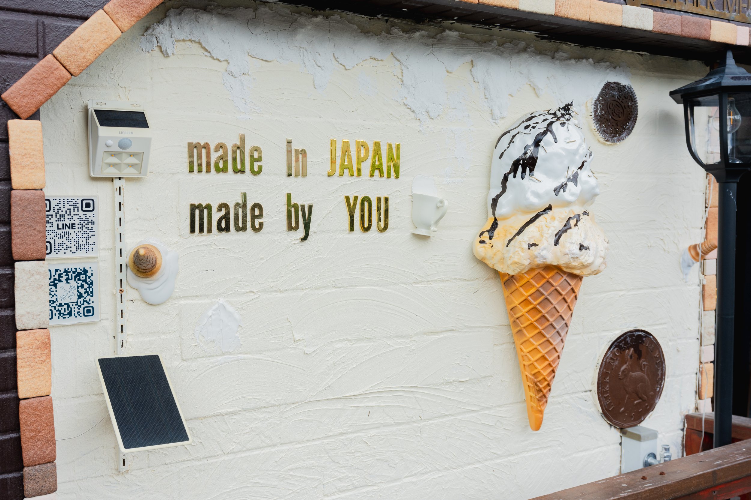 Decorative wall with a sign that says 'made in JAPAN made by YOU,' an ice cream cone sculpture, QR codes and various other decorative items.
