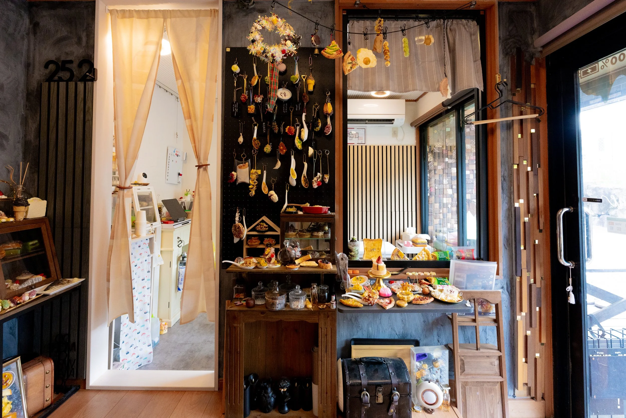 Interior of our workshop atelier melty 252 with decorative hanging items and baked goods on display, including cookies and cakes, with a door and window showing the outside.