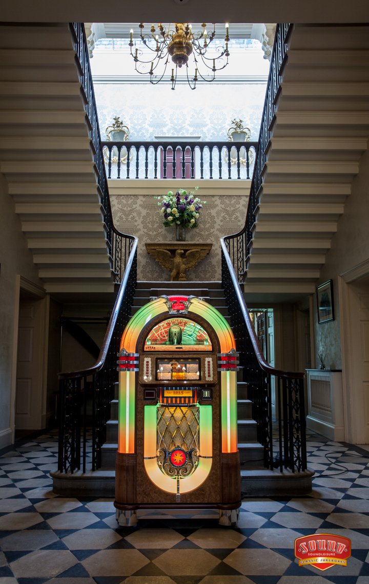 Vintage jukebox in a grand staircase entrance with checkered floor and chandelier.