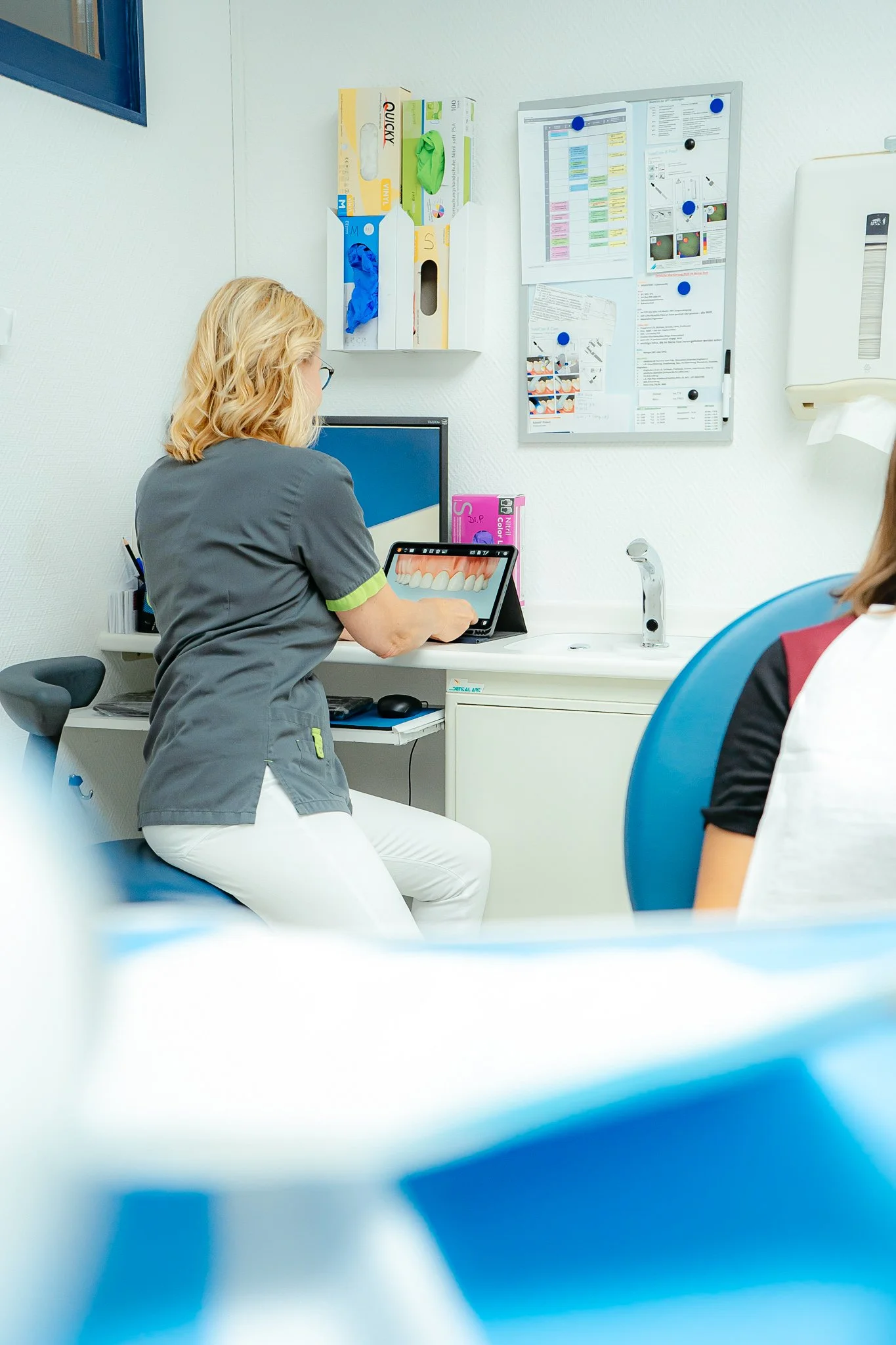 Zahnärztin zeigt einem Patienten digitalisierte Zähne auf einem Tablet im Behandlungsraum.