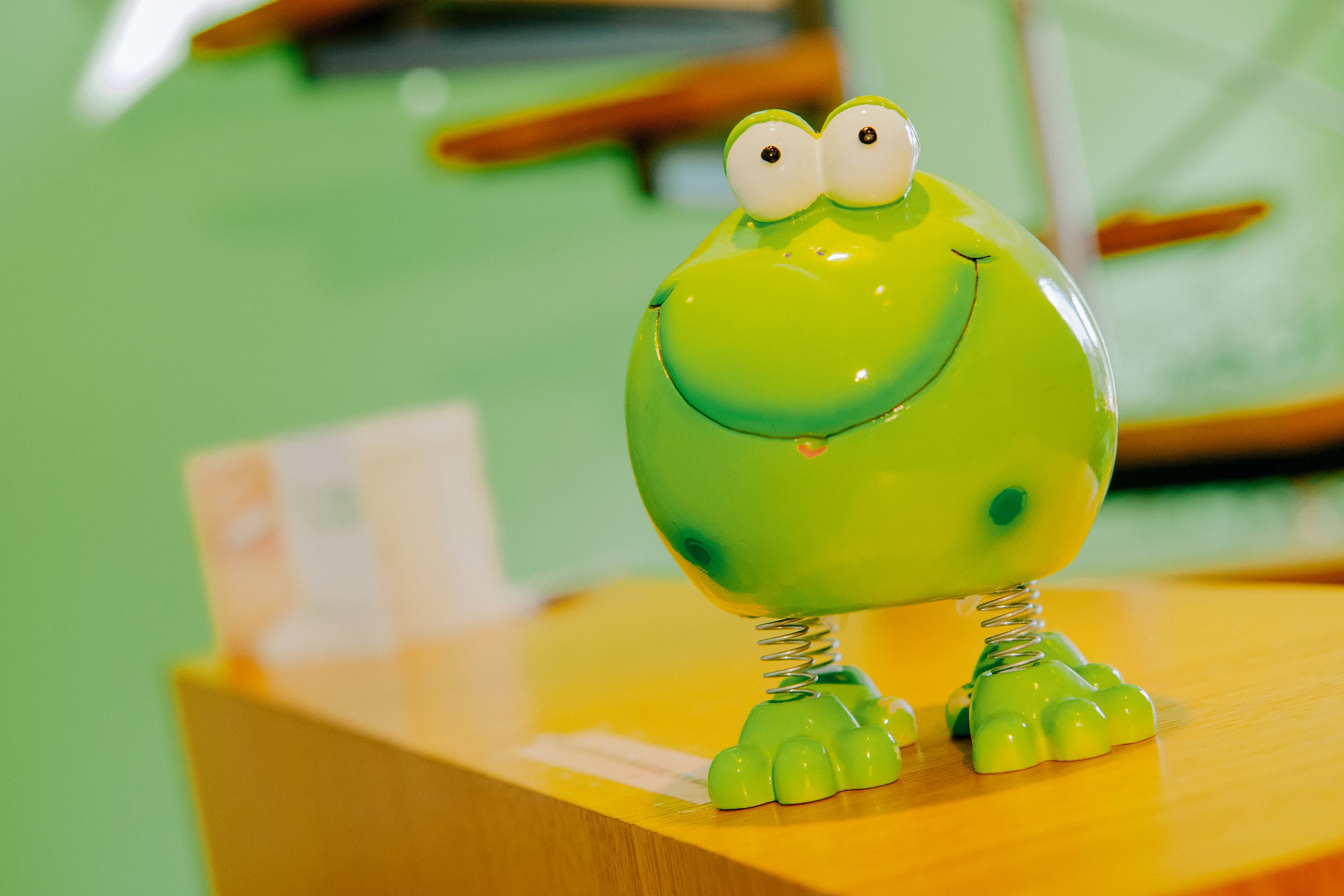 Eine grüne, lustige Spardose in Form eines Froschs mit großen Augen und einem Lächeln, auf einem Holztisch.
