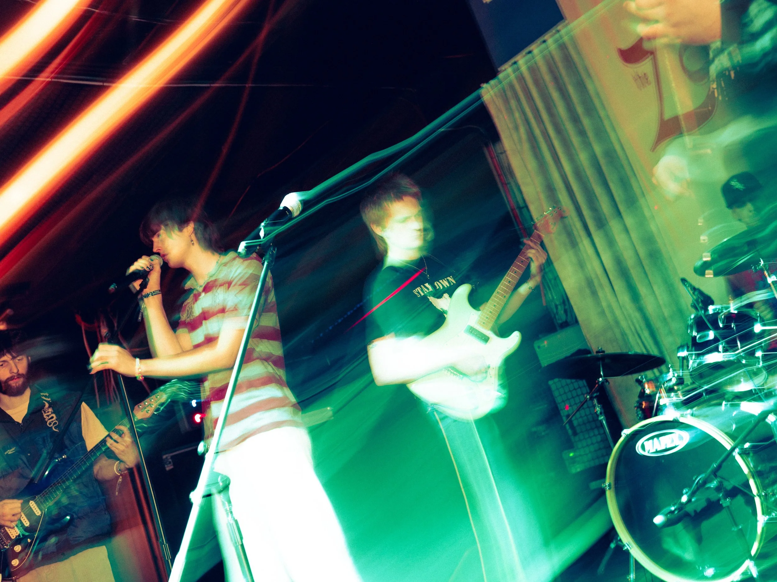 Band performing live with colorful stage lighting, featuring a female singer and guitarists.