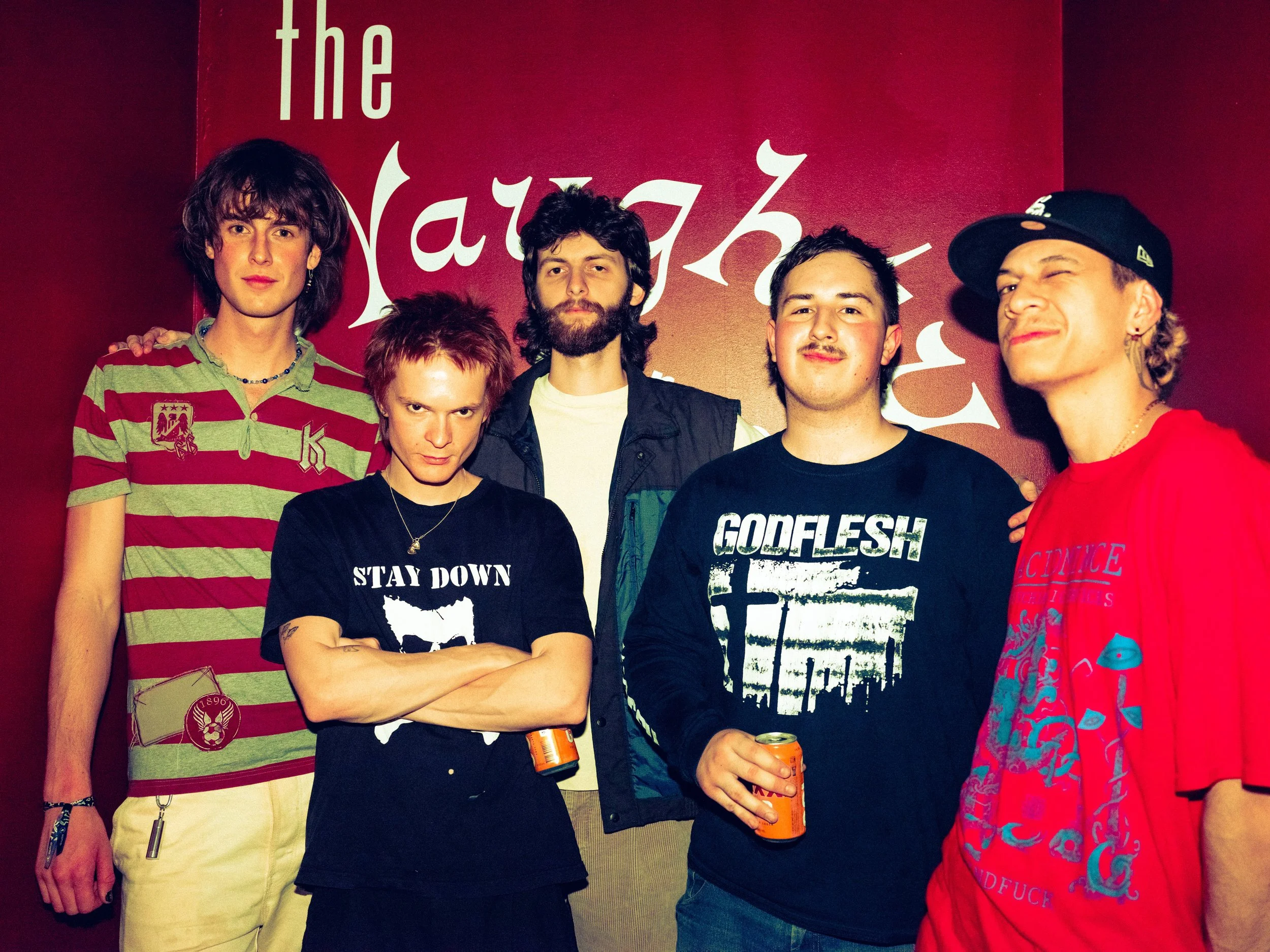 Group of six young people standing in front of a red background with white text, posing for a photo at a social event.