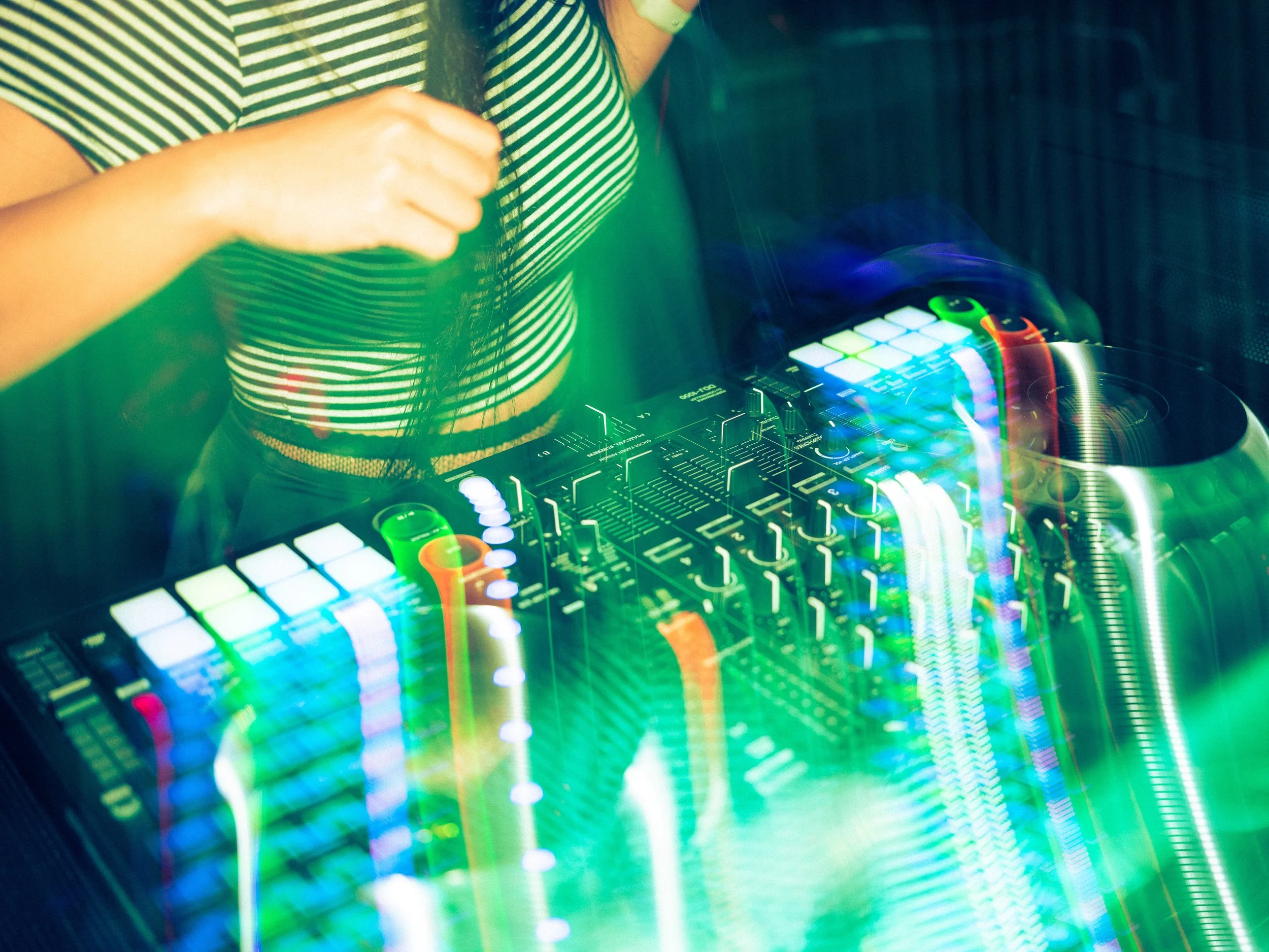 A person in a striped shirt using a DJ controller with colorful lights and rainbow reflections.