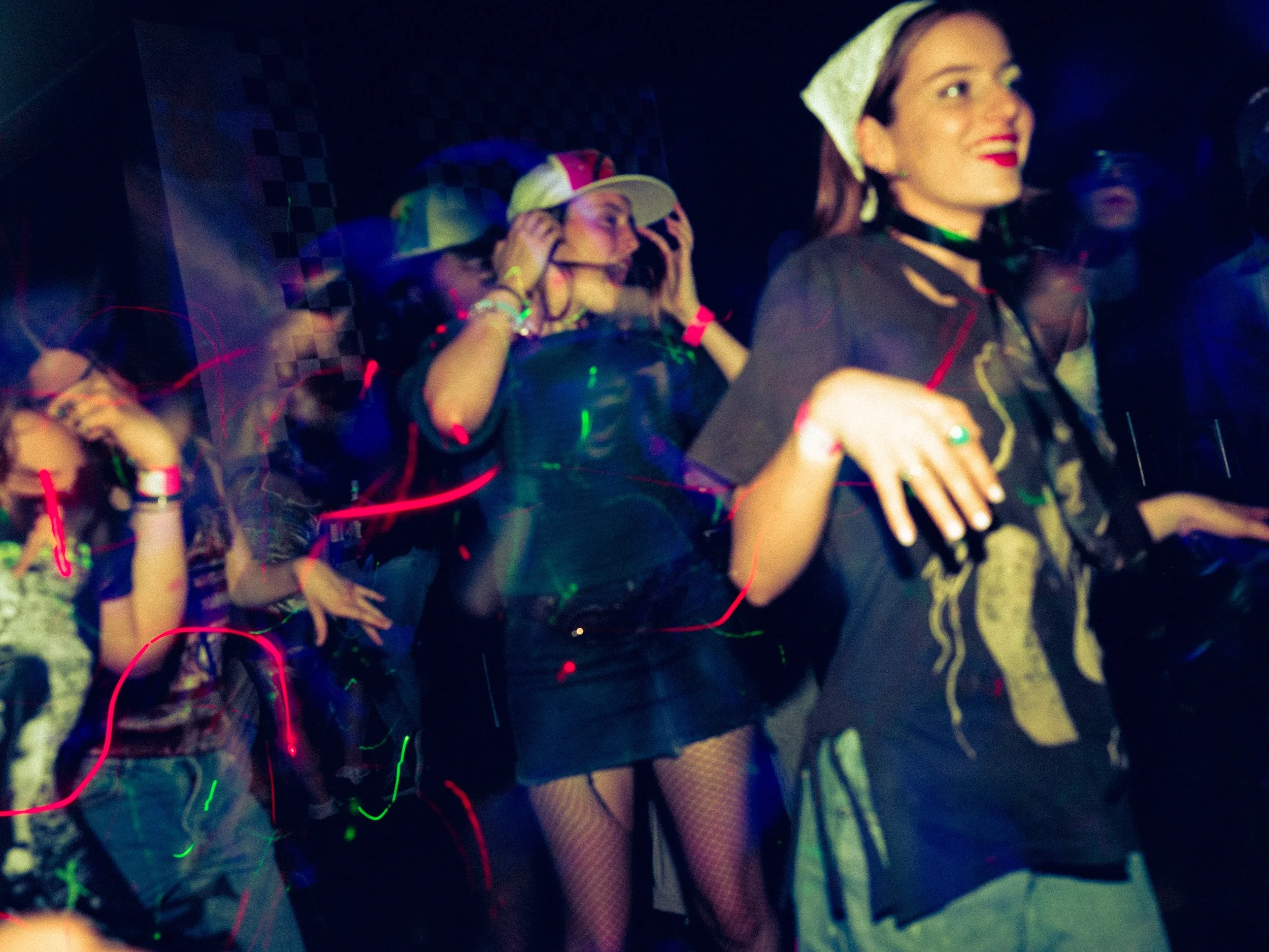 People dancing at a nightclub with colorful lights and a dark background.