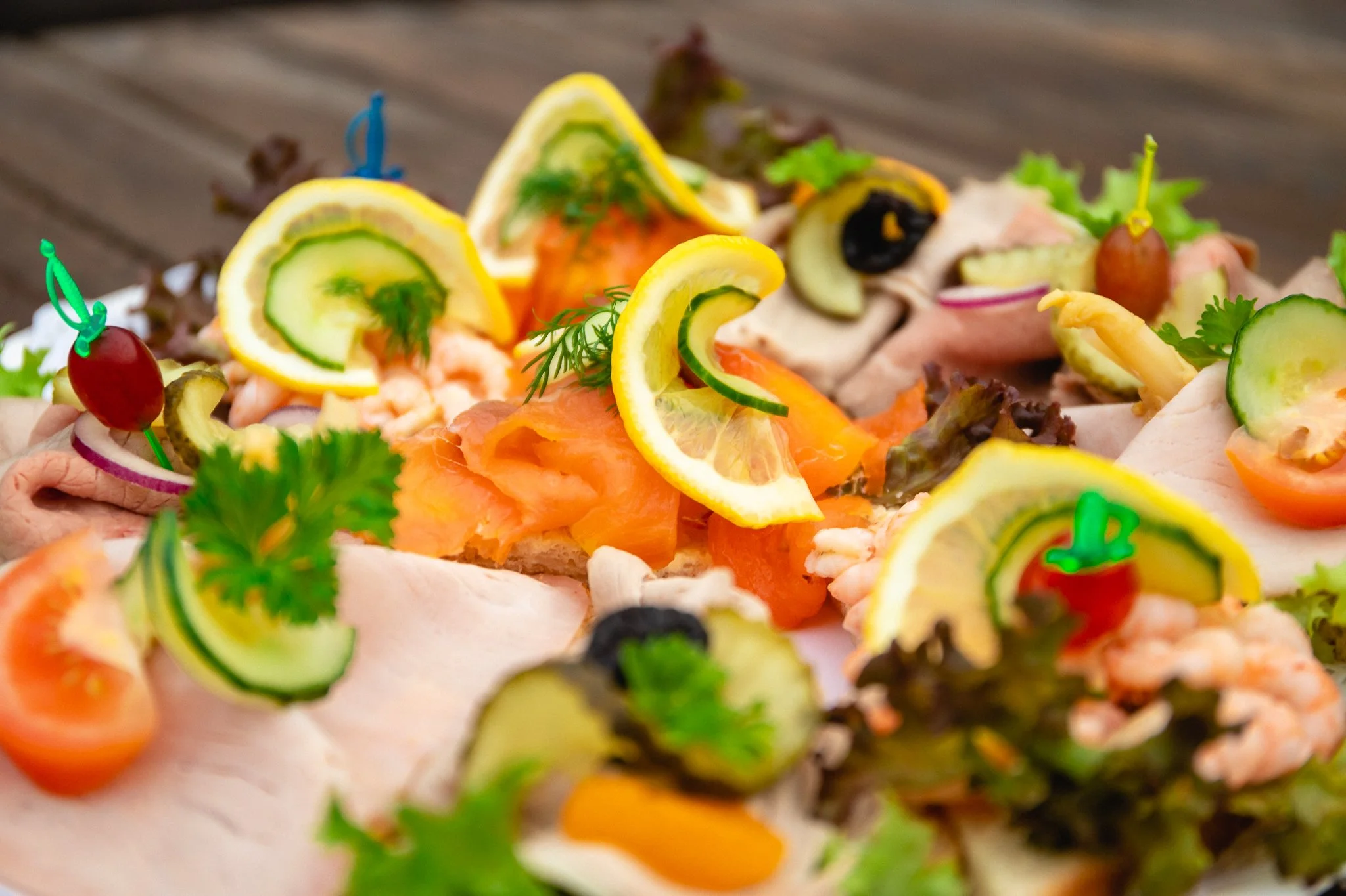 Rulletter med laks, kremost, agurk og paprika, pyntet med dill på et aluminiumsfat.