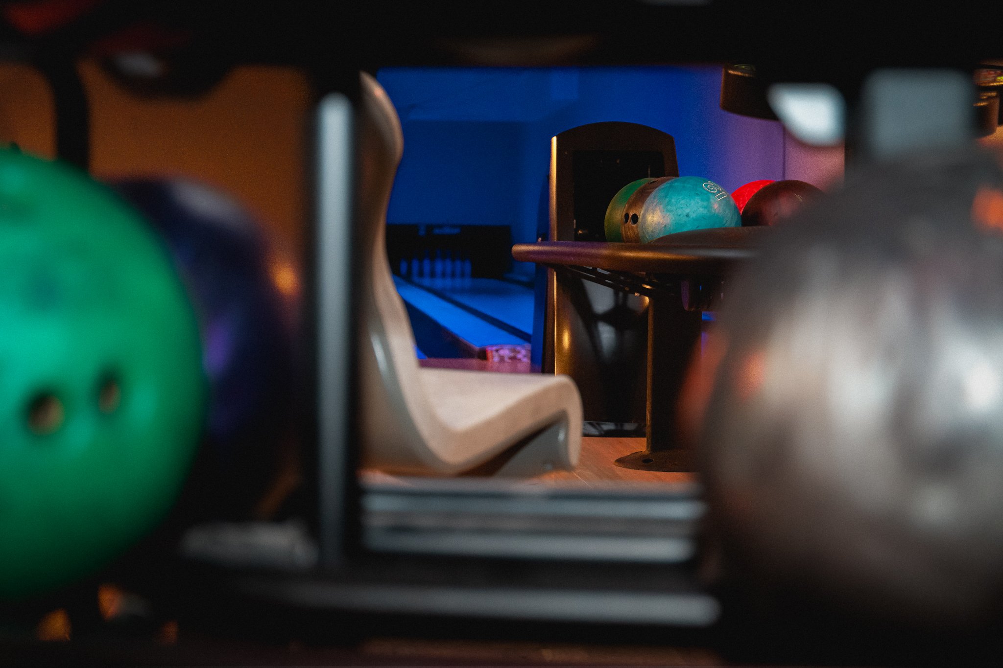 Innendørs bowlingbane med baller, sitteområde med sofa, og en skjerm. Betonggulv og vegglys