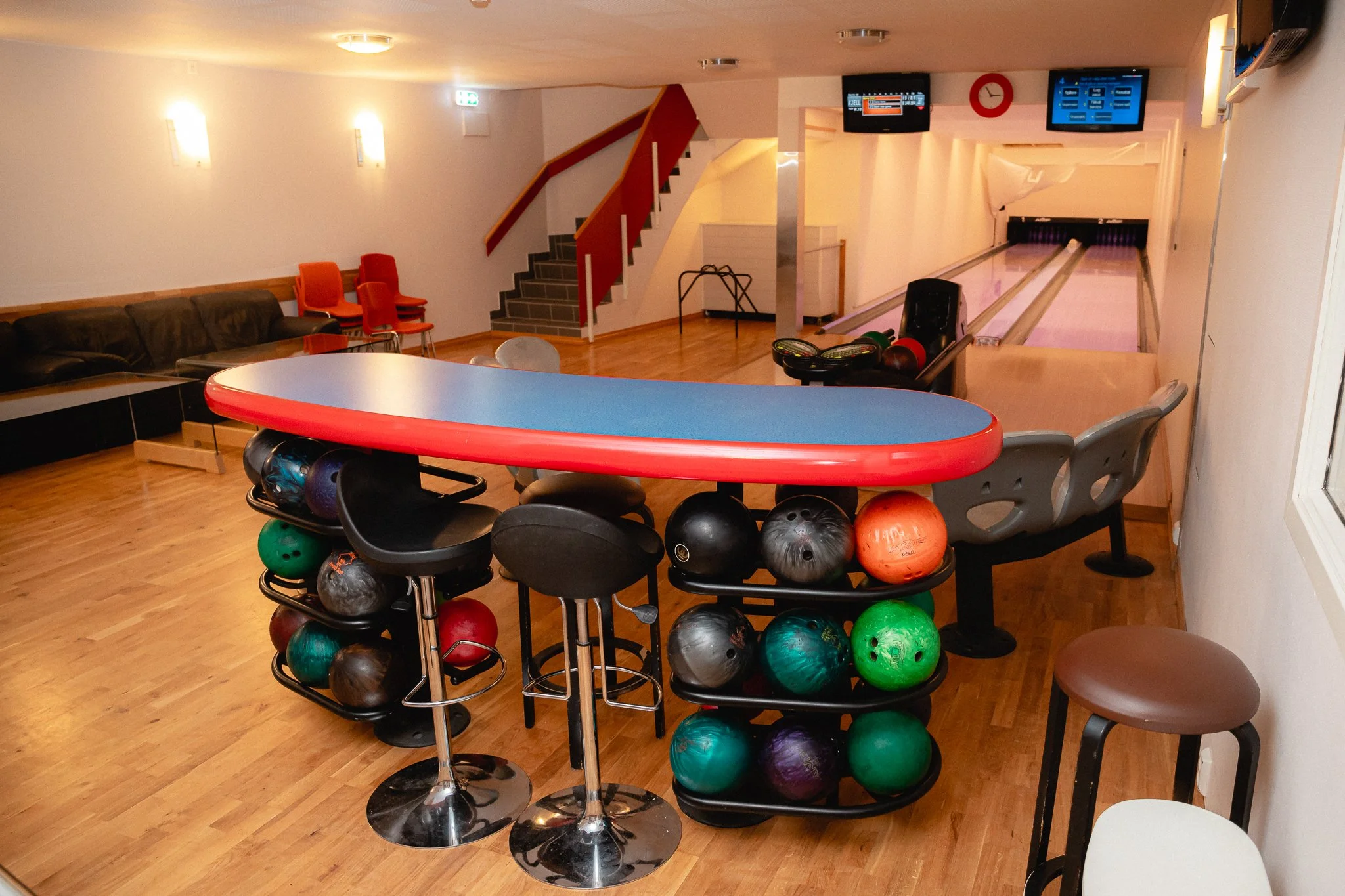Innendørs bowlingbane med bowlingkuler, sitteplasser, TV-skjermer og trapp.