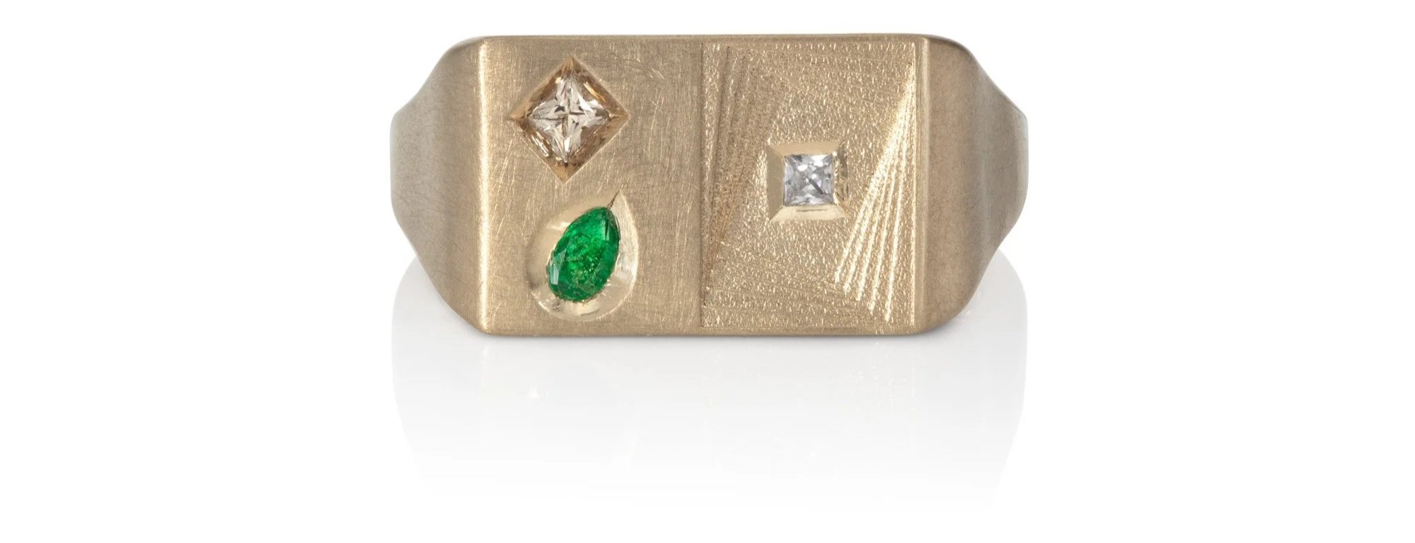 Gold signet ring with three gemstones: a diamond, a white gemstone, and an emerald.