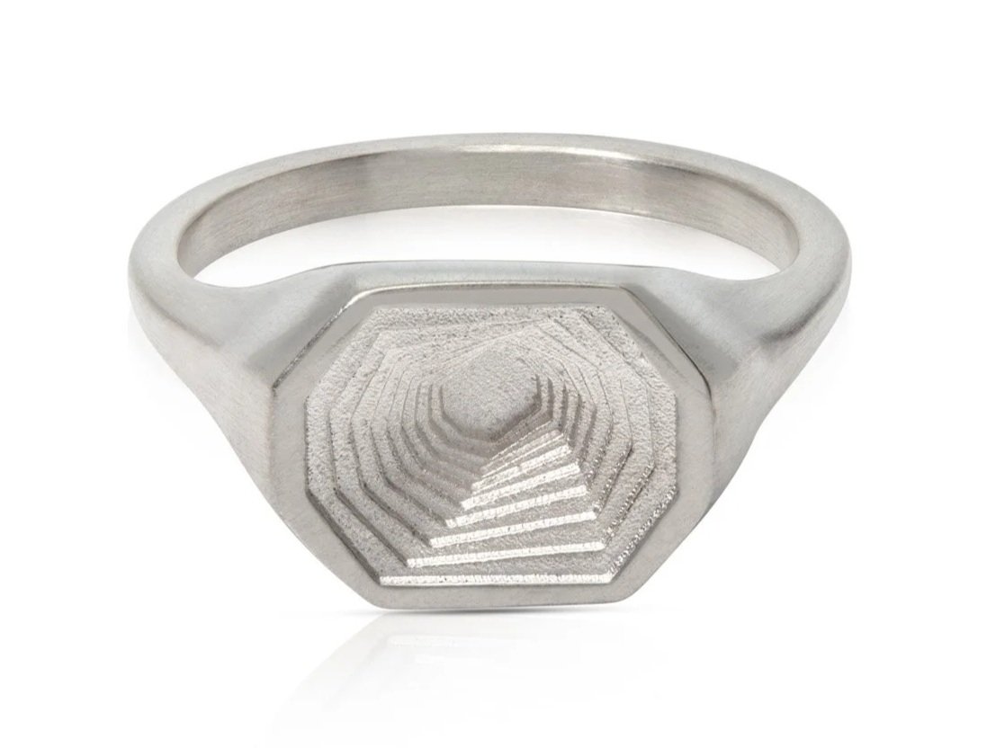 A silver signet ring with a raised hexagonal face featuring concentric hexagon patterns.