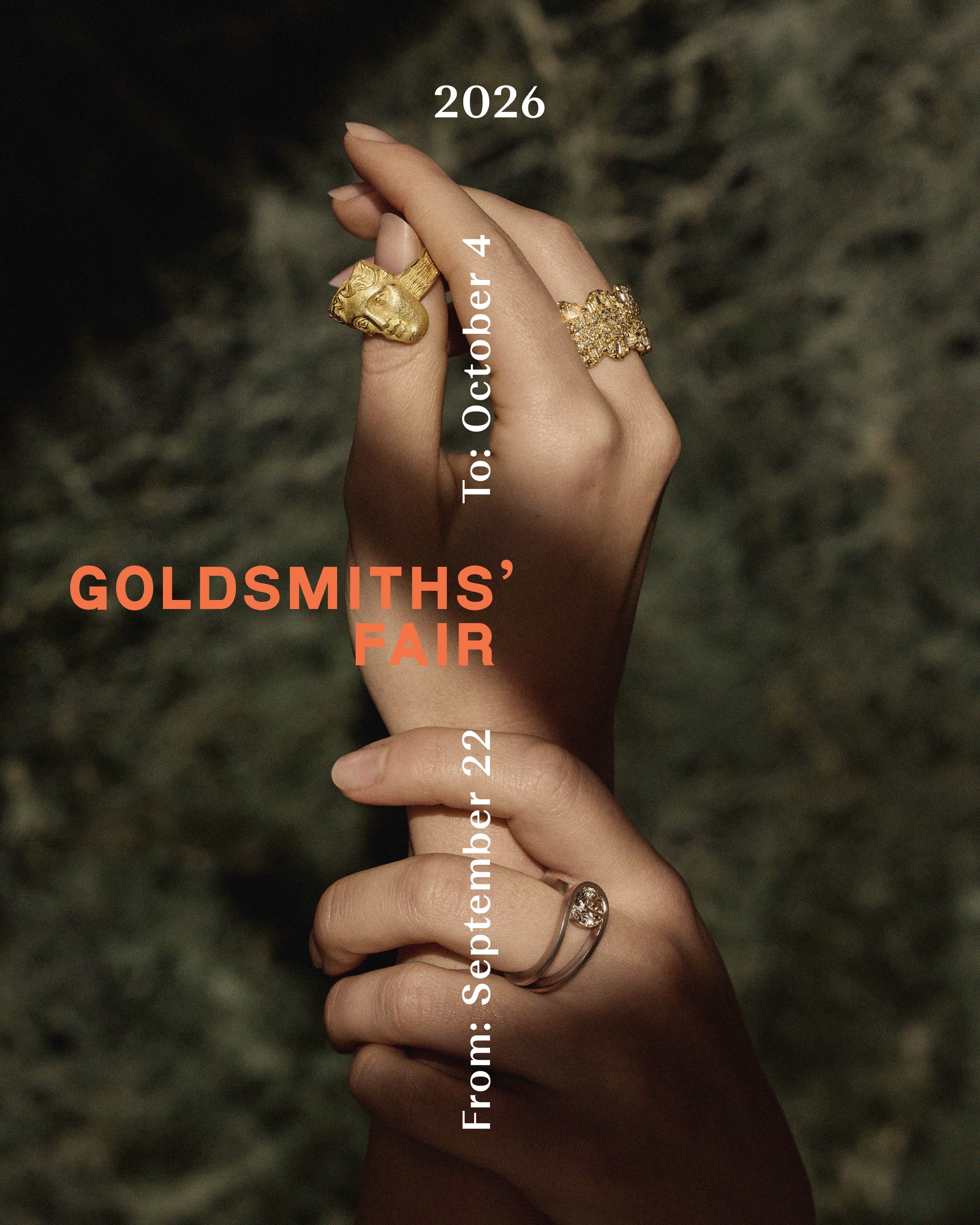 A person's hand with gold rings, one featuring a lion's head, against a dark background with text about a goldsmiths' fair.