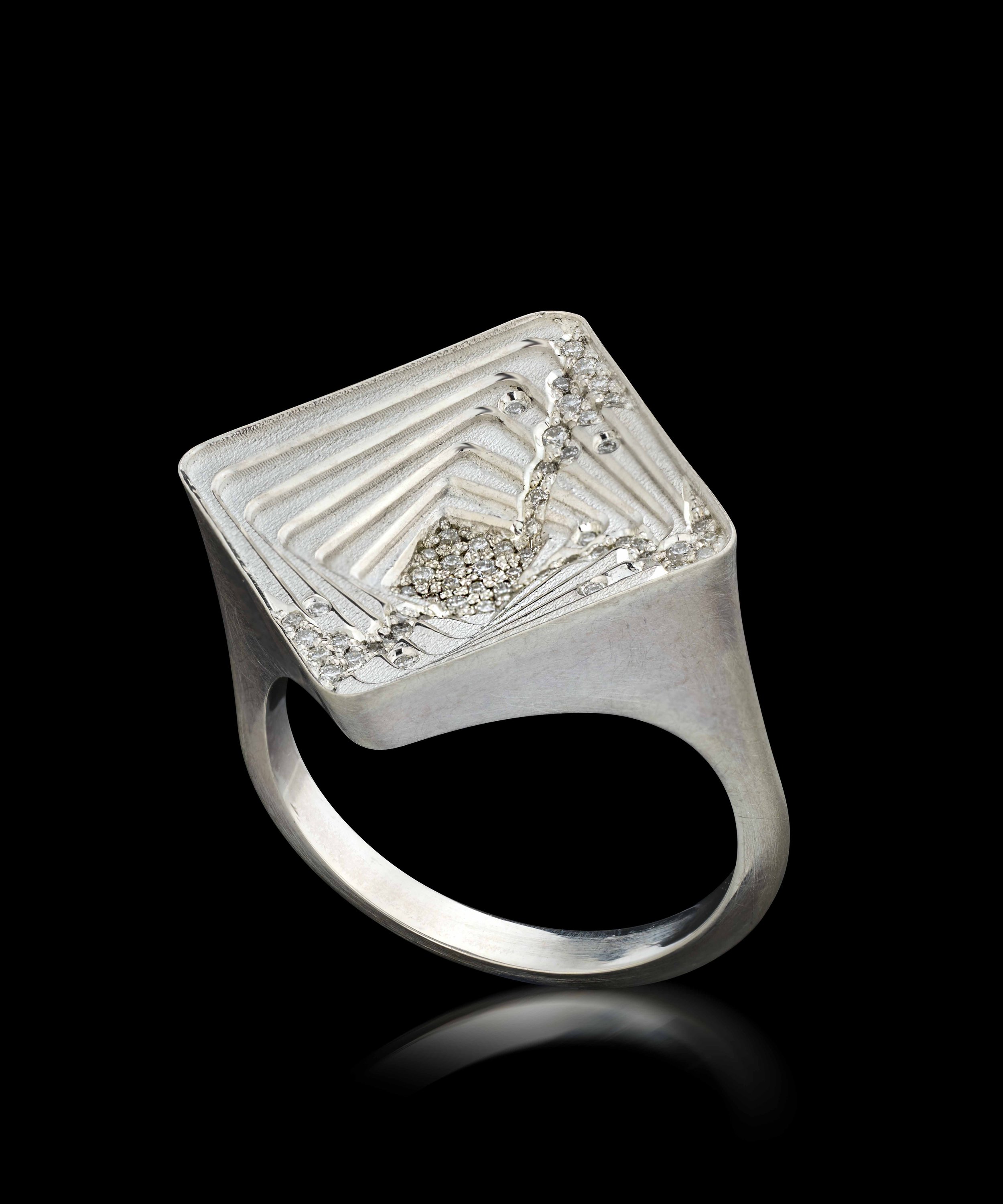 Close-up of a silver ring with square top setting containing small diamonds, viewed from above against a black background.