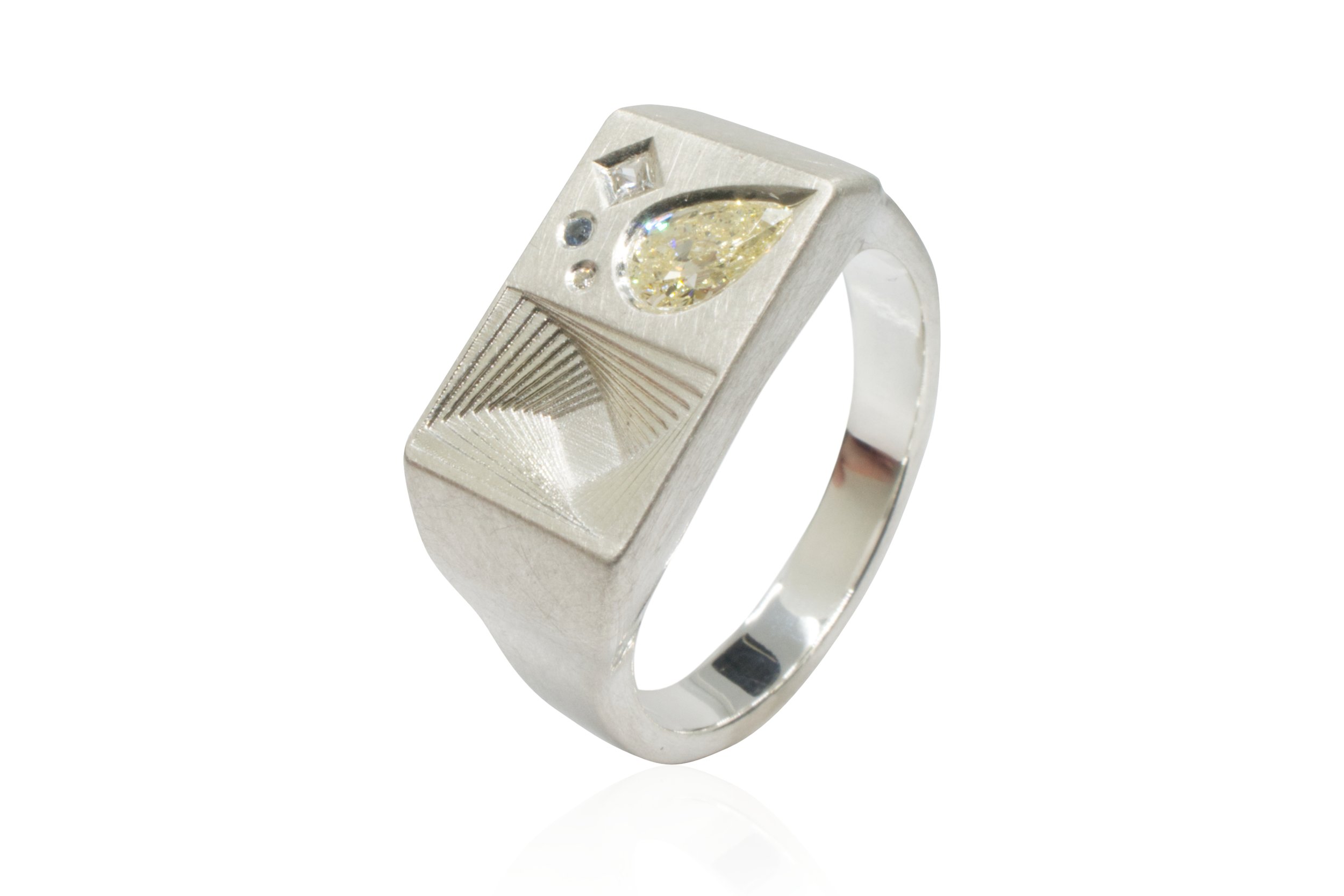 A silver ring with a rectangular face featuring a large teardrop-shaped yellow gemstone and two smaller accent stones, with engraved lines on the face.