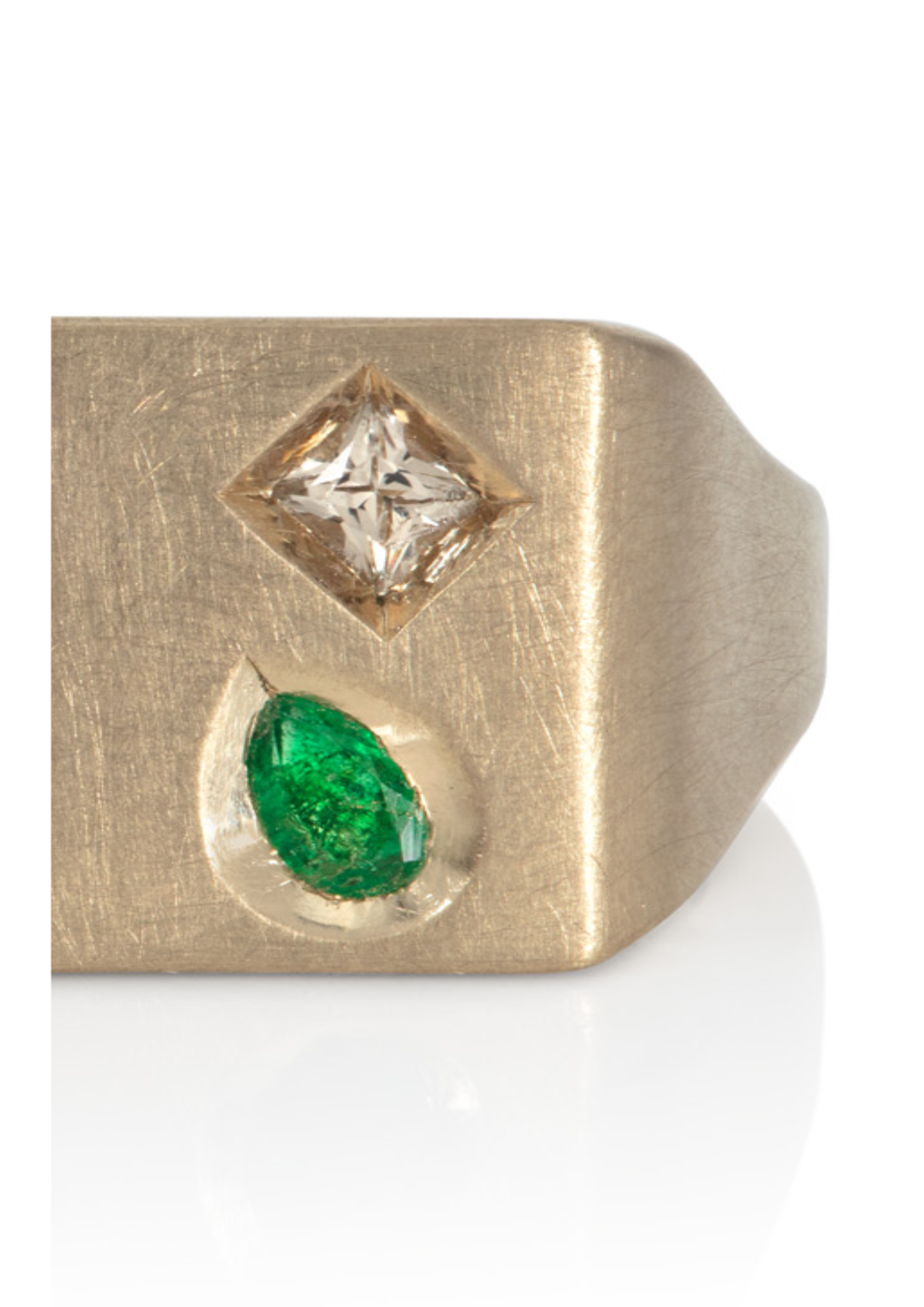 Close-up of a gold ring with a square diamond and a green gemstone set in the band.