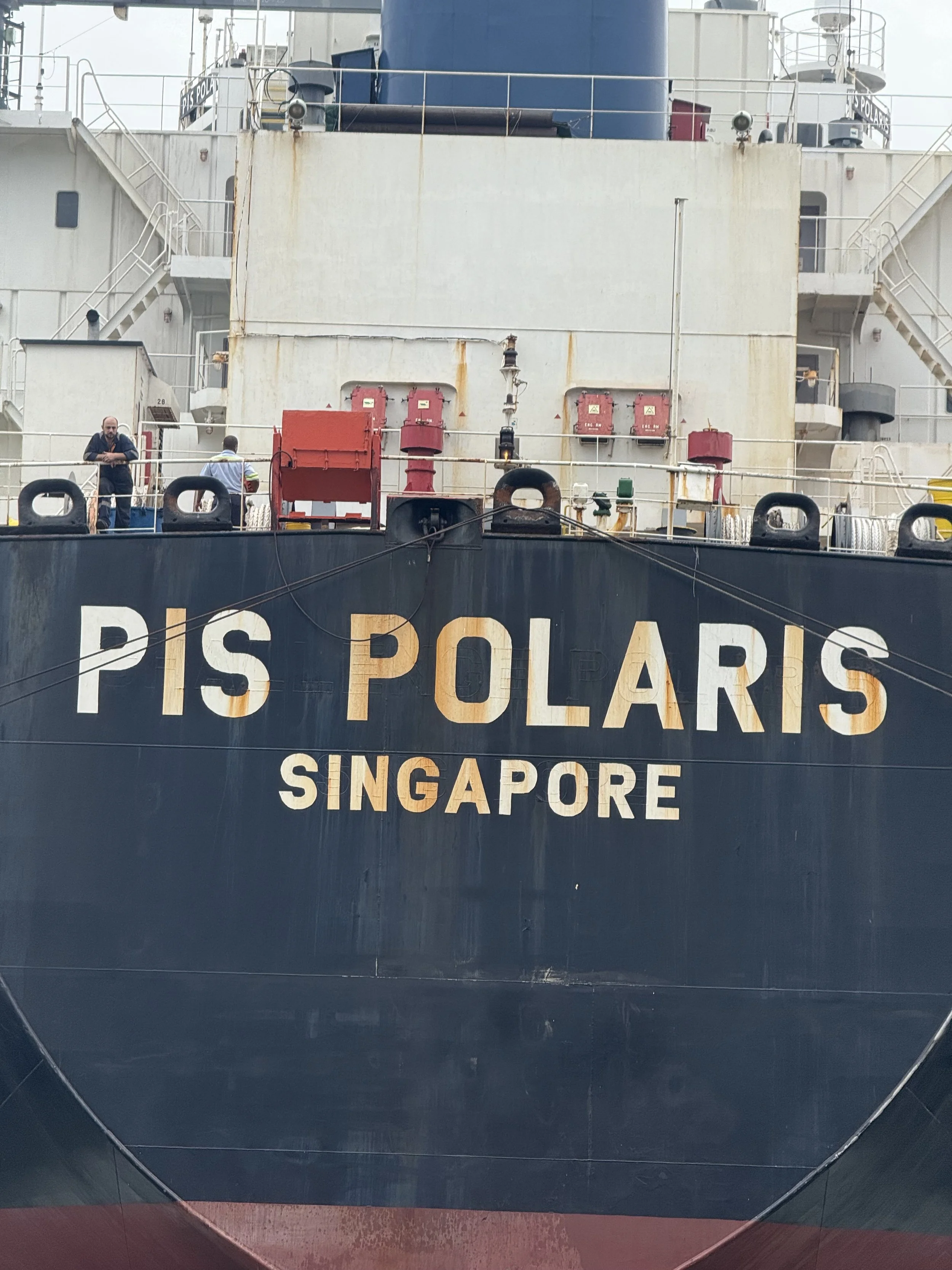 Close-up of the front of a large ship named 'PIS POLARS SINGAPORE,' with various equipment and crew members visible on the deck.