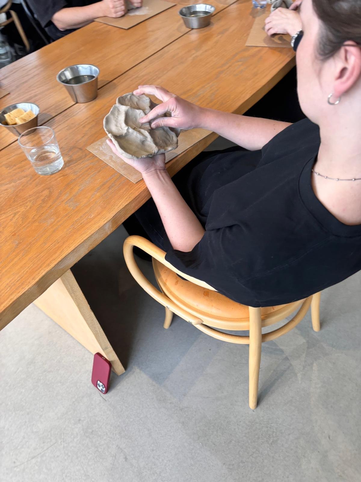 Person som håller i en lergods som de troligen har skulpterat, sittande vid ett träbord med andra personer.