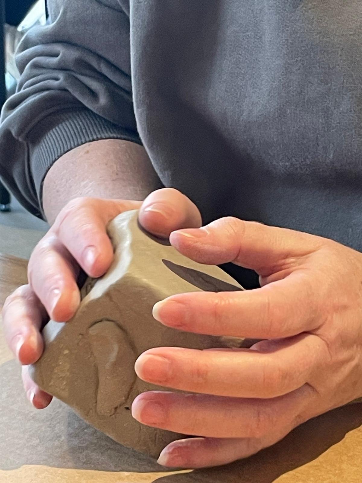 En person som formar en boll av lera eller annat modelleringmaterial.