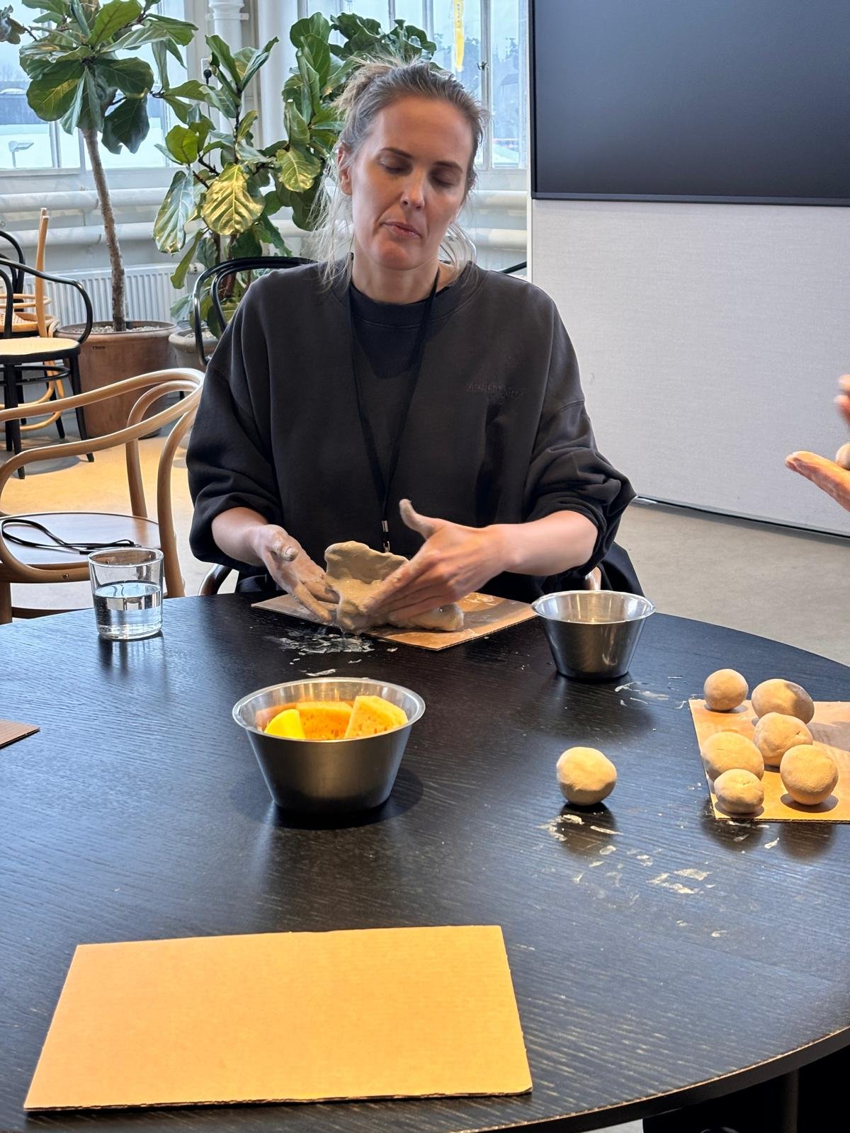 En kvinna som arbetar med deg på ett bord, med lera framför henne, i ett glatt utrymme.