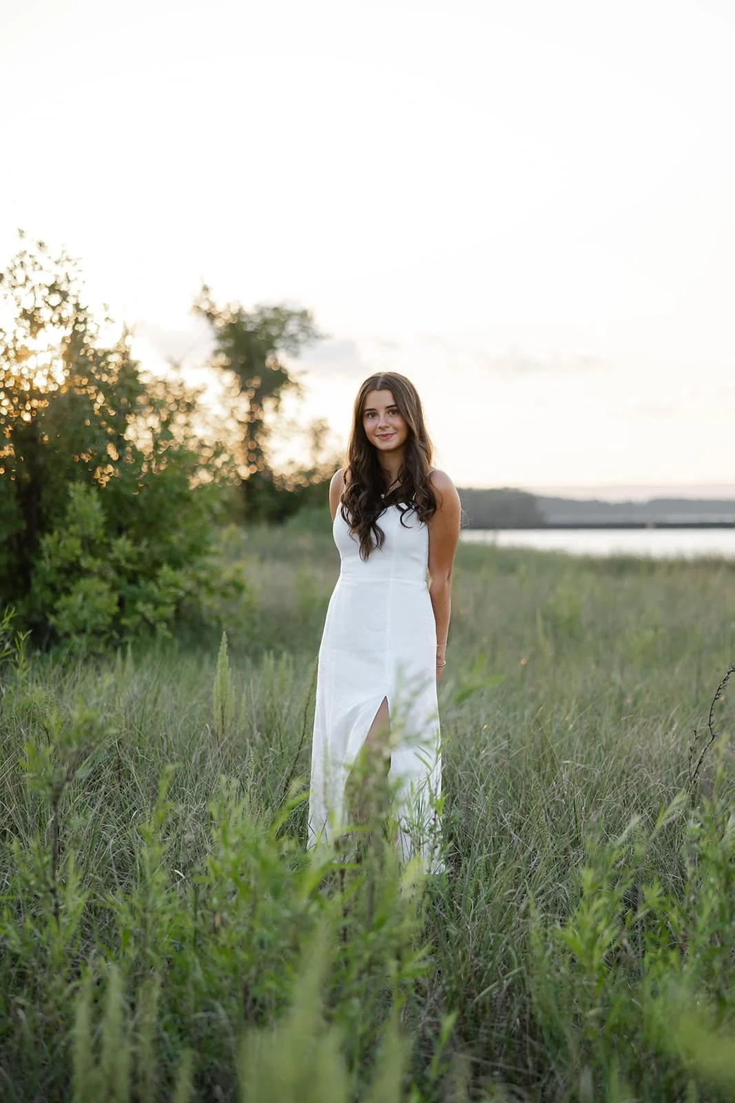 Young woman in a white dress standing in a grassy field at sunset.