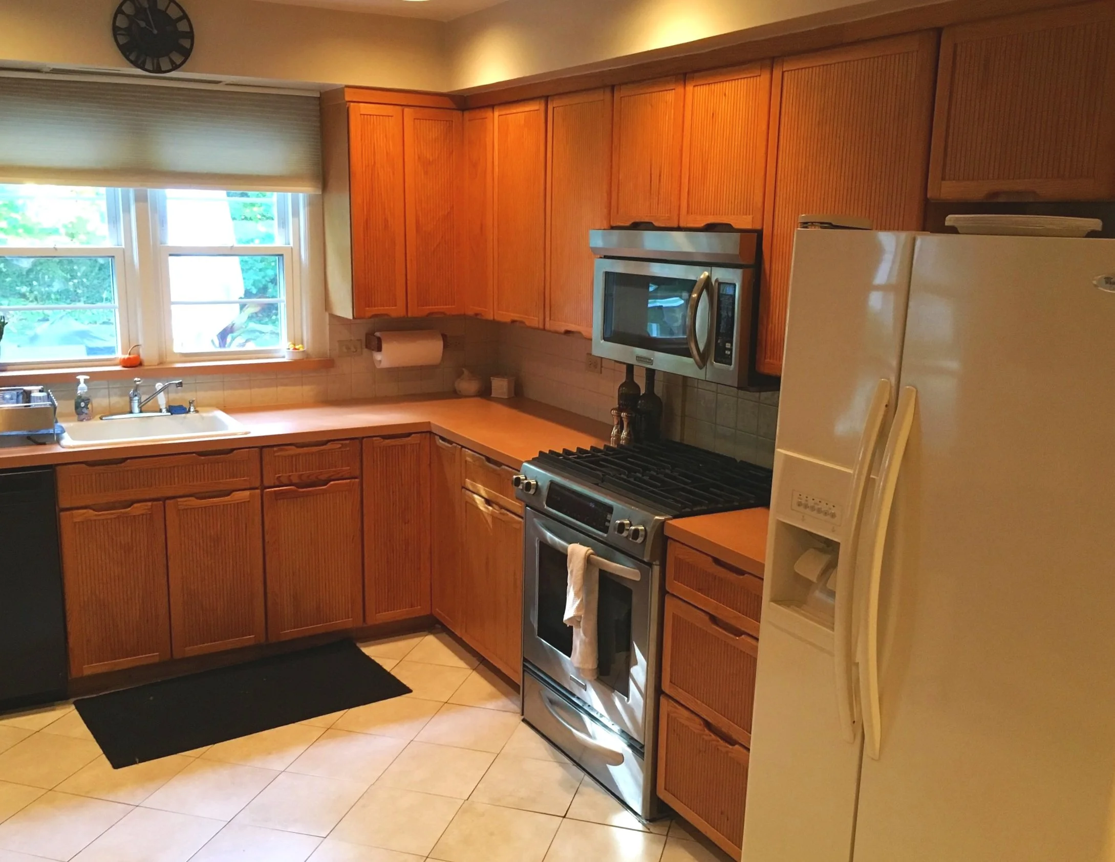 A kitchen with wooden cabinets, a white refrigerator, a stainless steel stove, microwave, and a sink under a window.