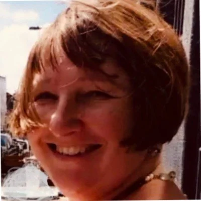 Close-up of a woman smiling outdoors with her hair covering part of her face.