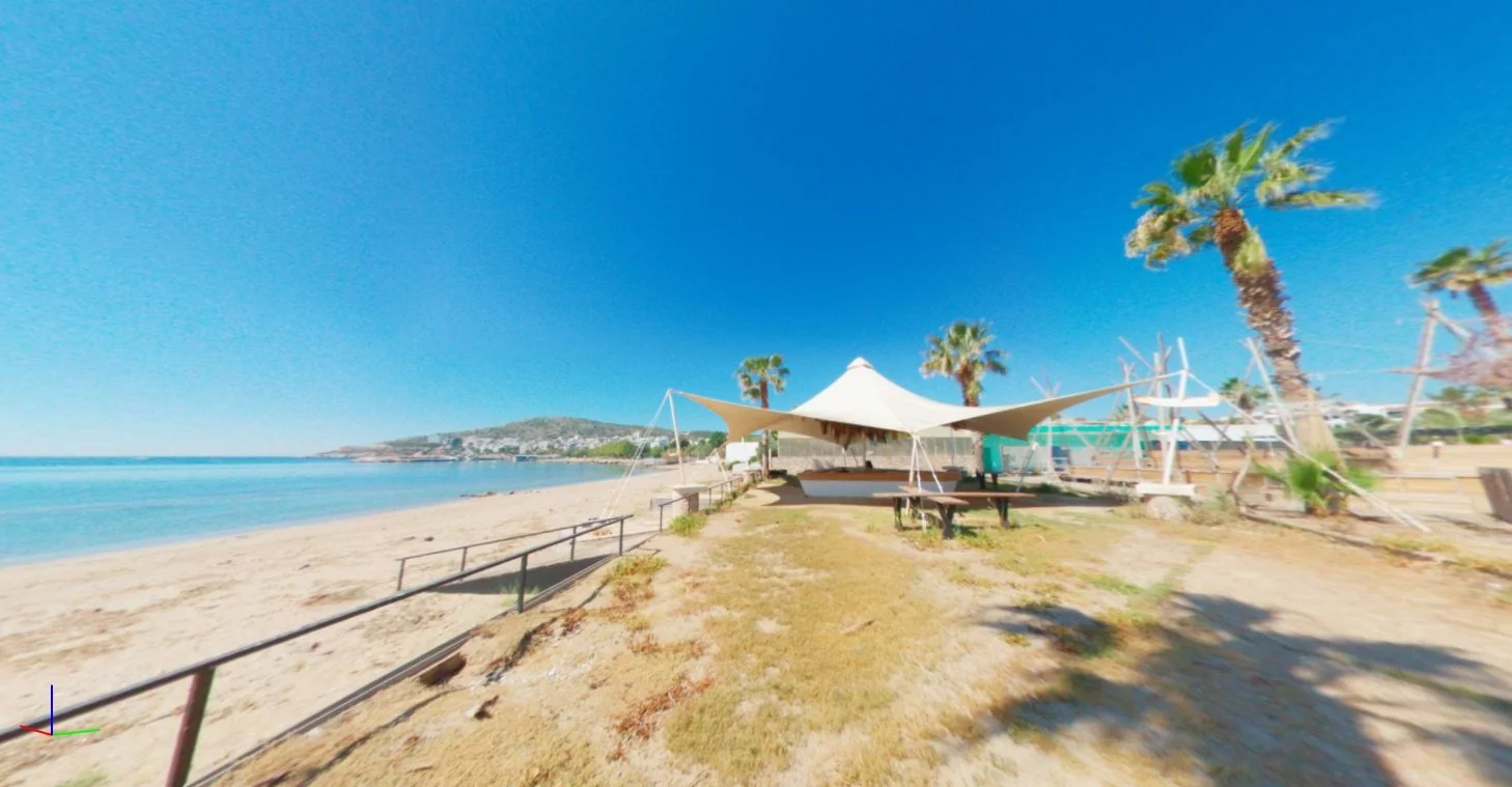 Beach with a sand shoreline, blue sky, some palm trees, and a white tent structure in the middle.