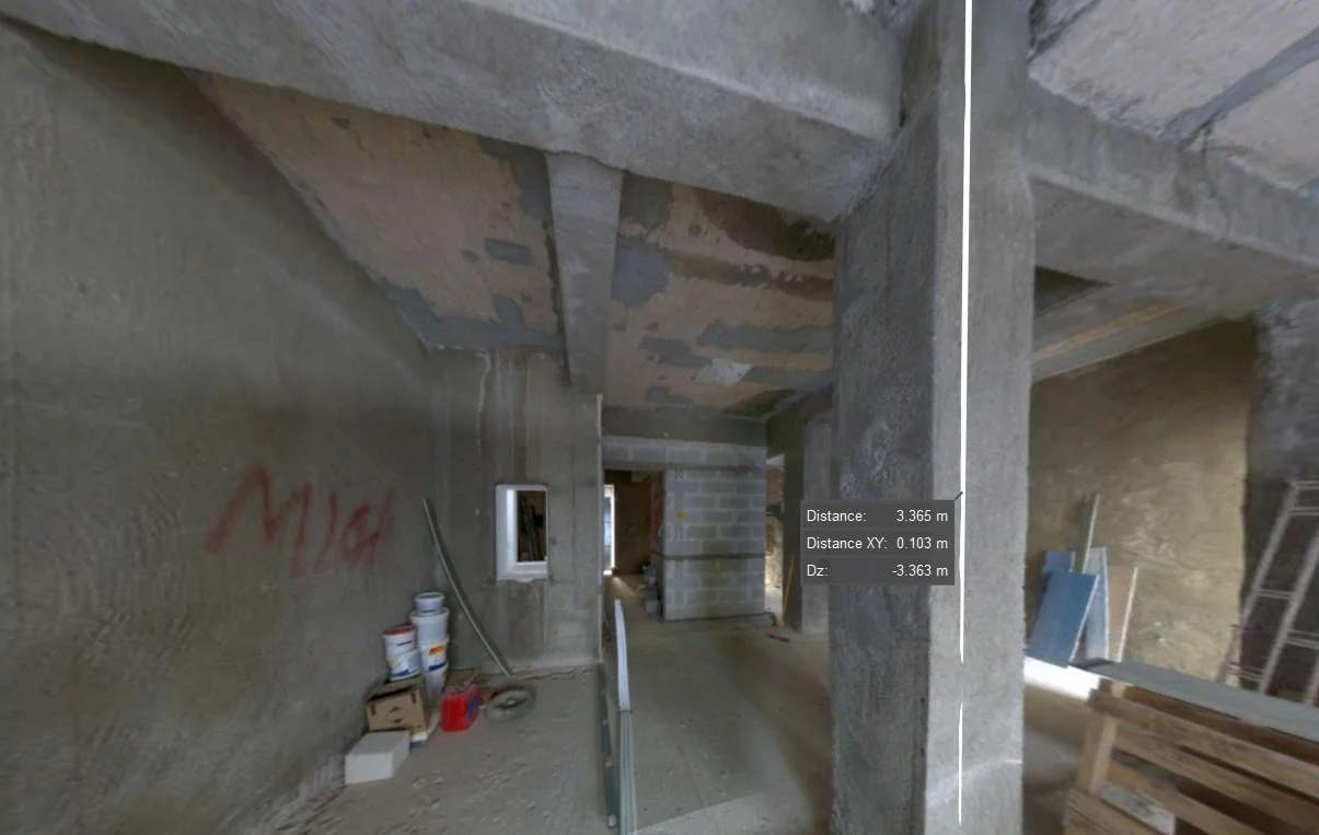 Interior view of a construction site with concrete walls and exposed beams, construction materials, and buckets on the floor.