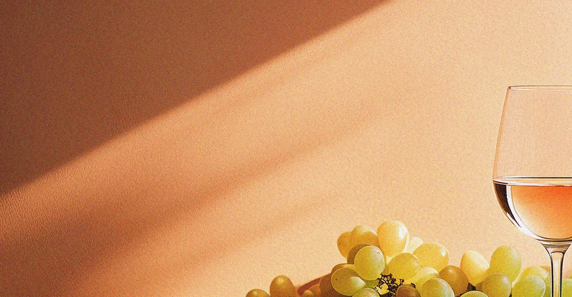 A glass of rosé wine, a bunch of green grapes, and a shadowed background.