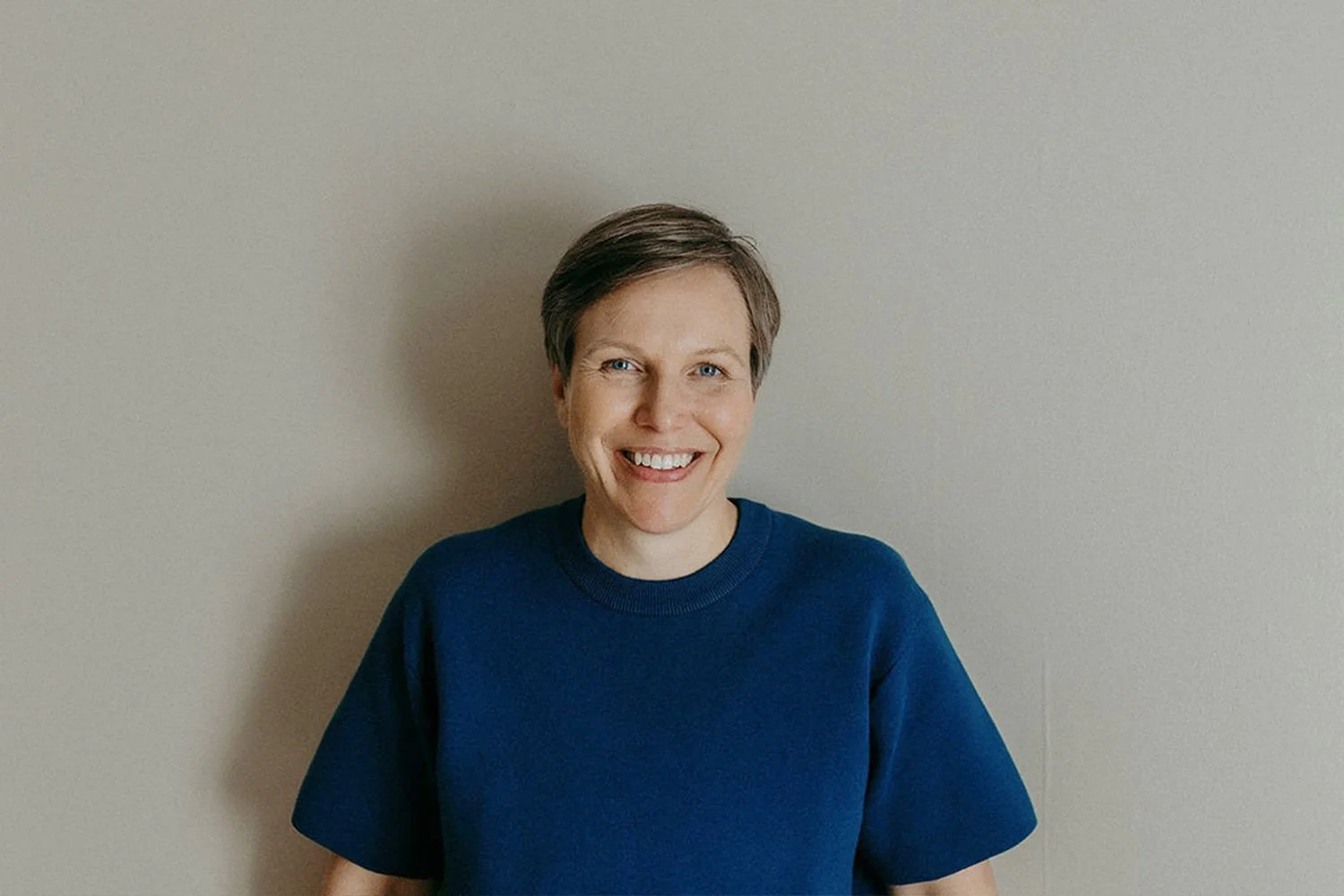 Niina Sjöblom hymyilee nojaten vaaleaan seinään.