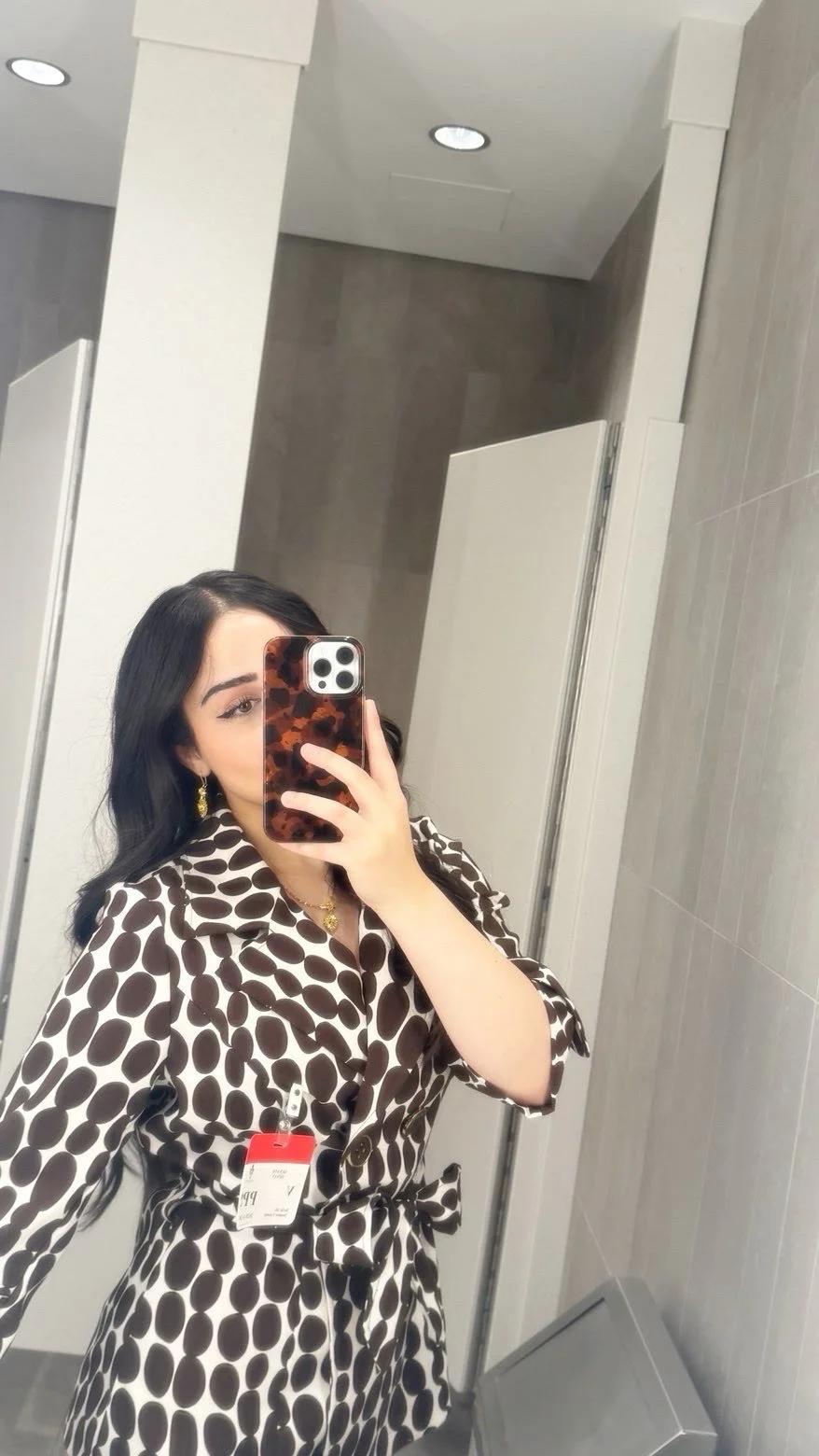 young woman in patterned top taking selfie with phone covering half of face