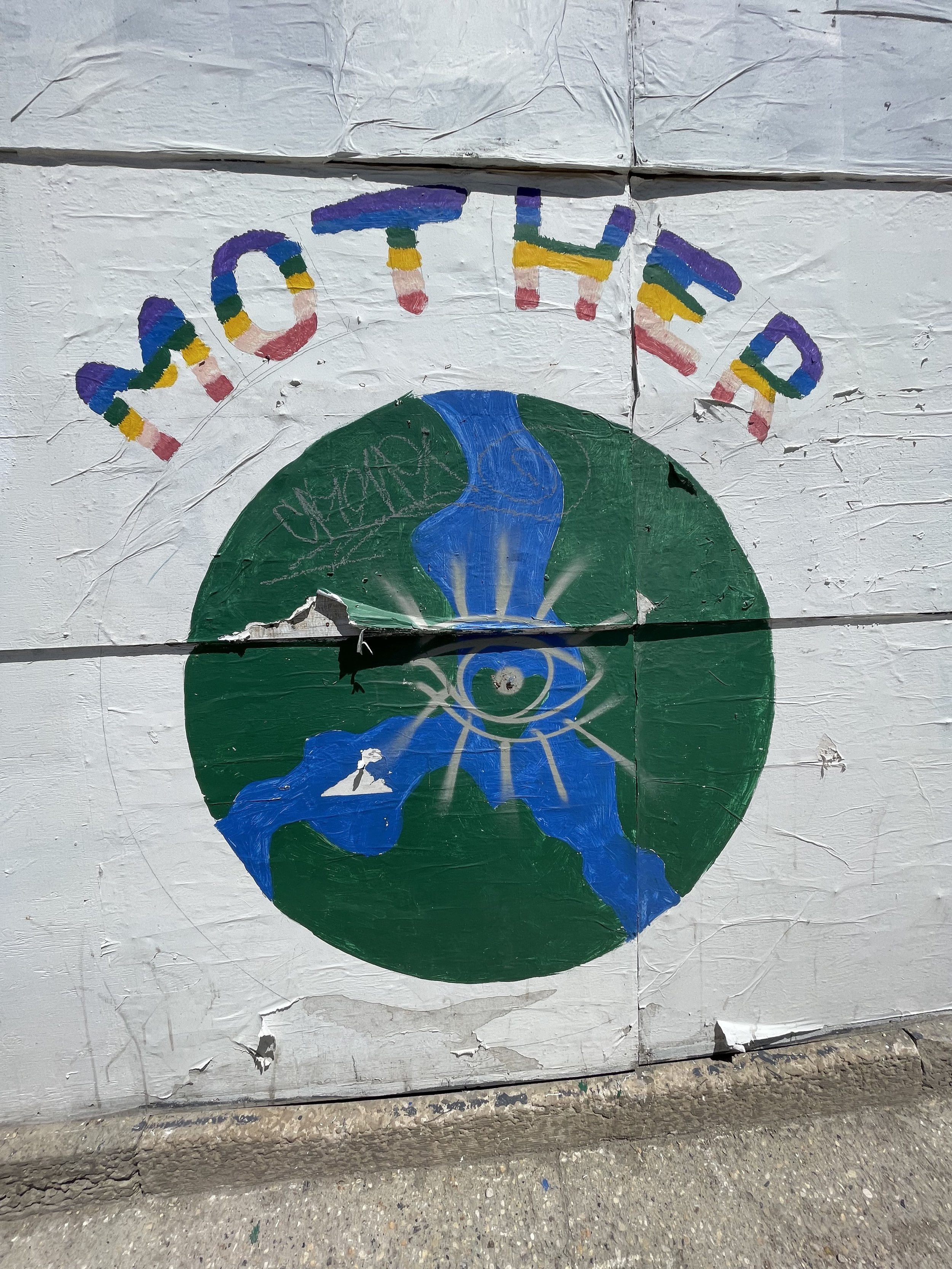 Painting on a wall depicting the Earth with a blue river flowing through it, a white mountain, and a stylized eye with rays above it. The words 'Protect the Earth' are painted above.