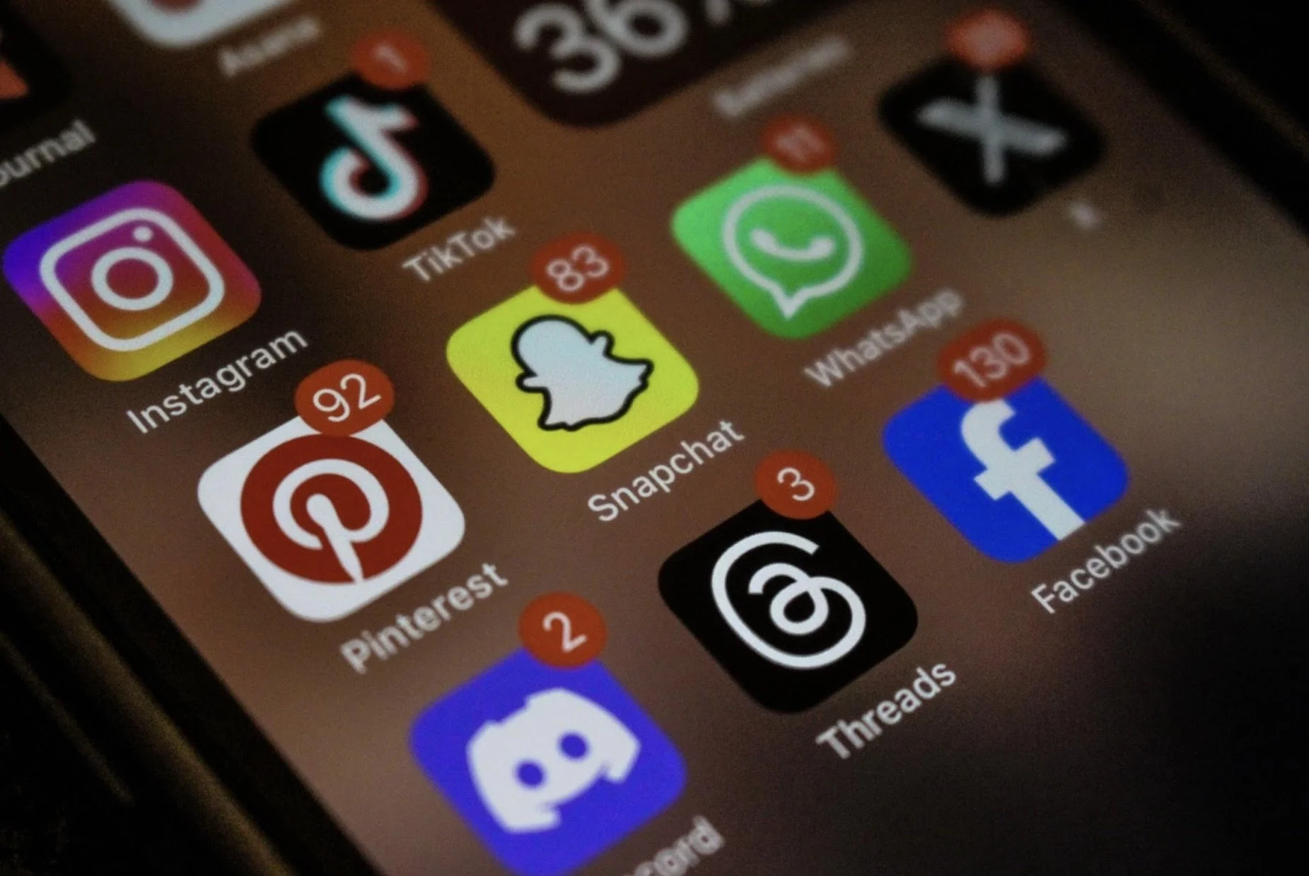 Close-up of a smartphone screen displaying various social media app icons including Instagram, TikTok, Snapchat, WhatsApp, Pinterest, Threads, Facebook, and Discord, with notification badges showing the number of unread messages.