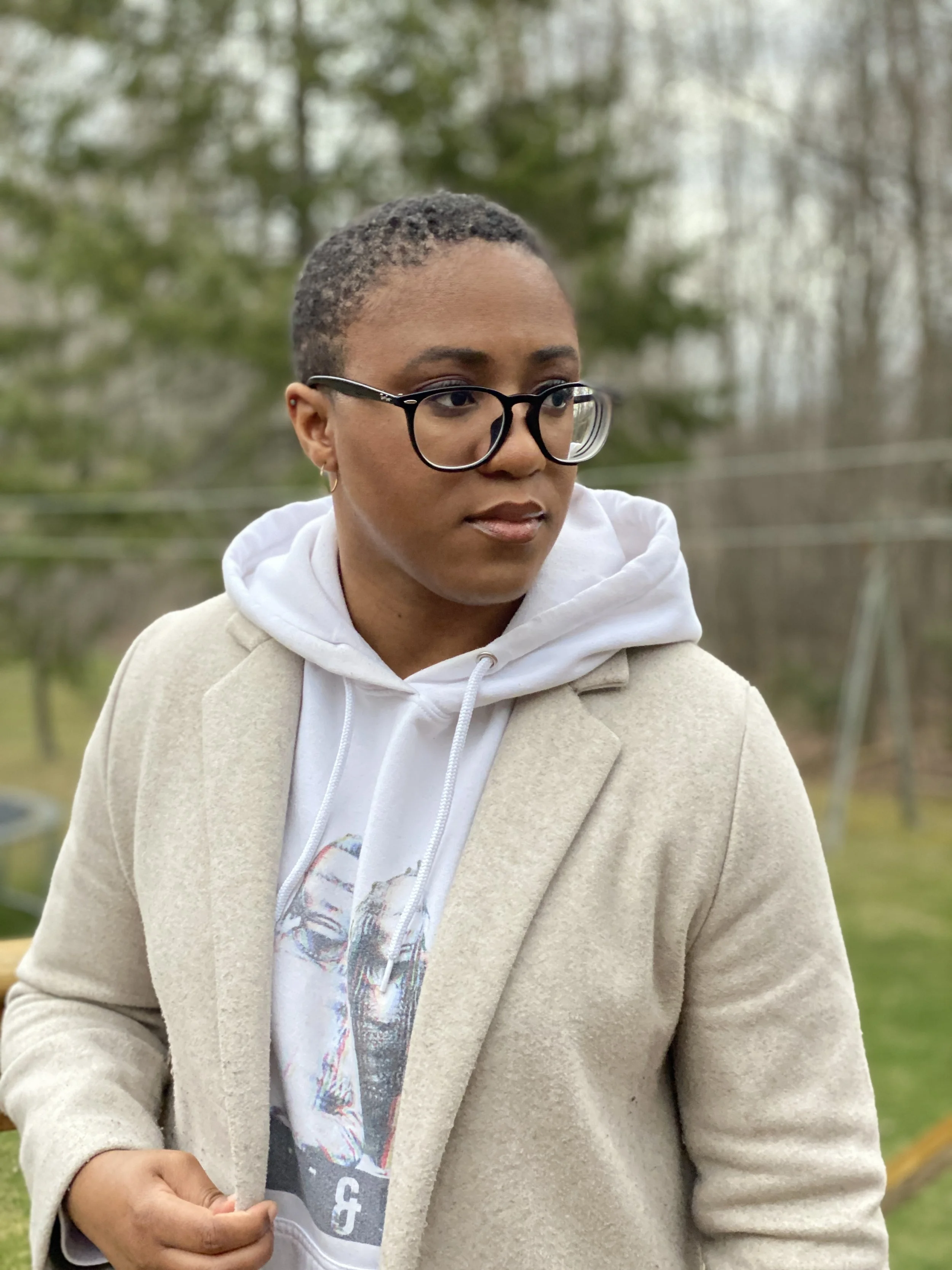 A woman with glasses and buzz cut hair in a sweatshift and jacket