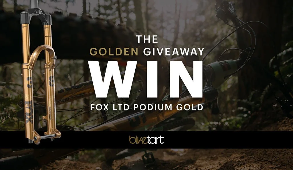Gold-colored Fox limited edition podium fork giveaway promotion, featuring a mountain bike in a forest background with the text "The Golden Giveaway. Win Fox LTD Podium Gold."