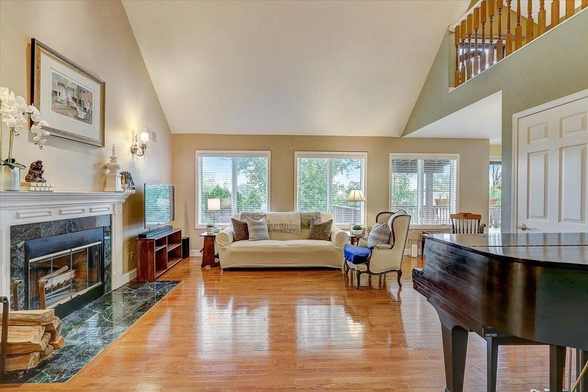 Living room with hardwood floors, a fireplace, a sofa, armchairs, a TV, and large windows with views of greenery outside.