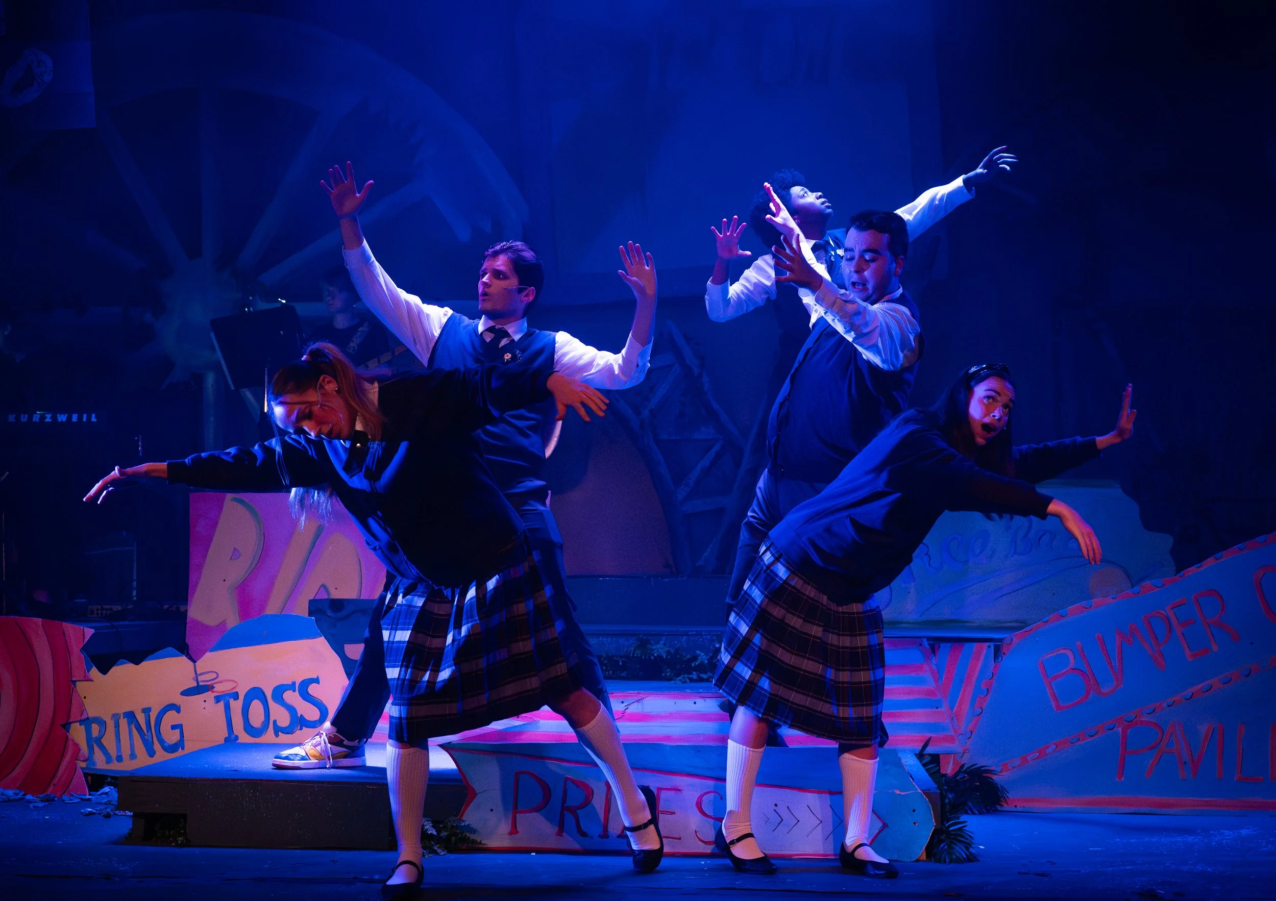 Young performers in school uniforms dancing on a stage with bright colored signs and props.