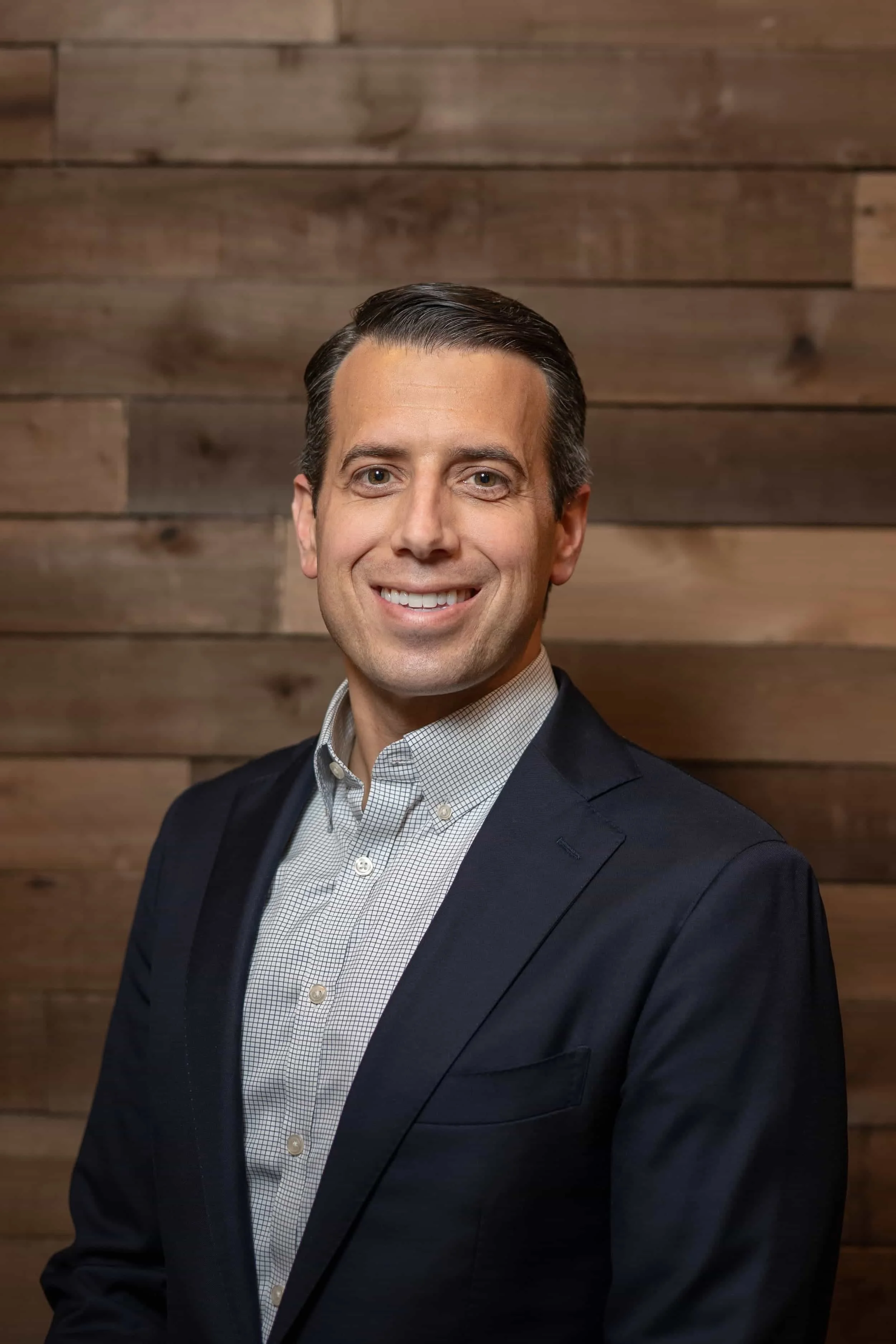 Professional man in suit smiling against a wooden wall background.