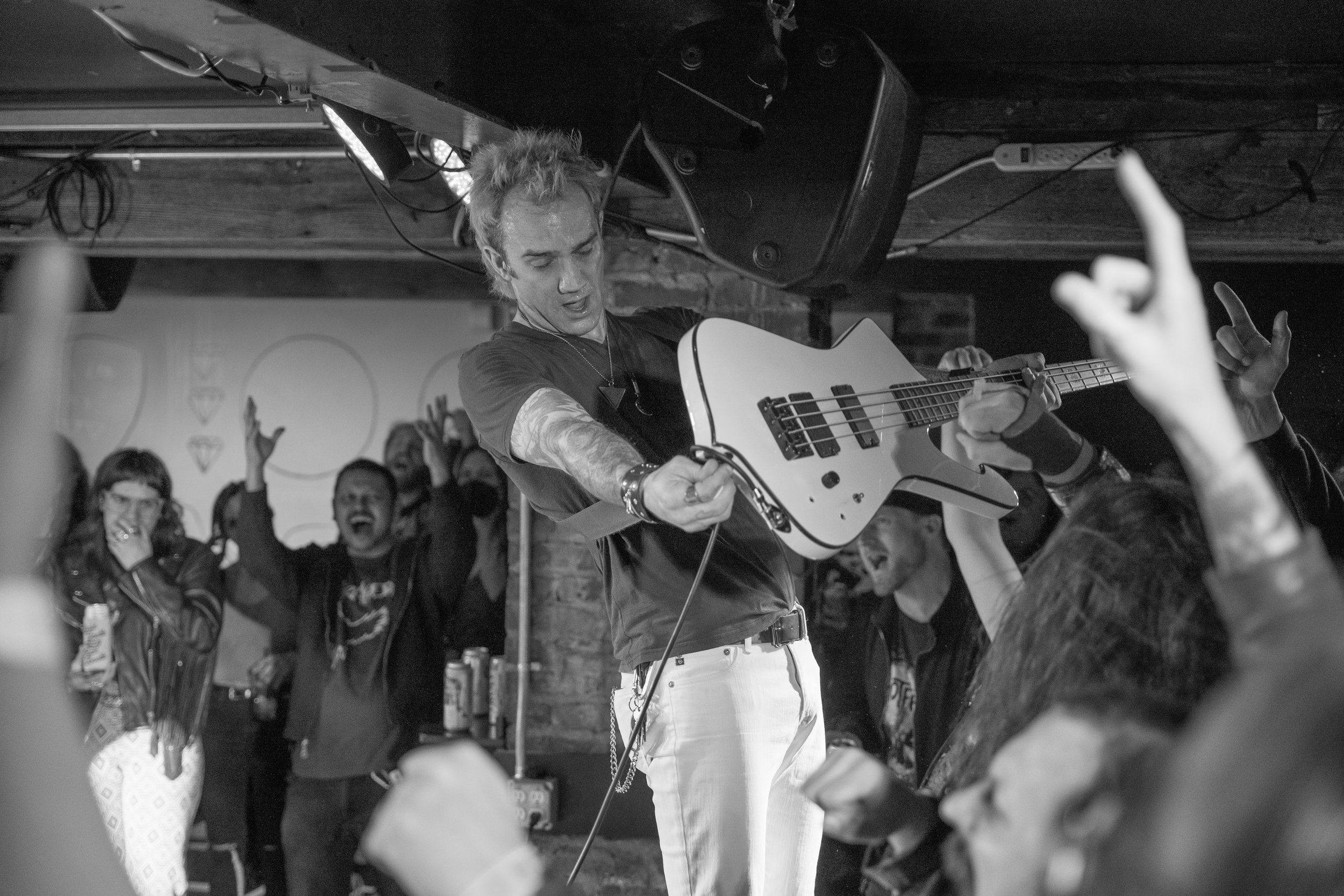 A live concert scene with a male guitarist on stage, holding an electric guitar, surrounded by an enthusiastic crowd with some raising their hands and cheering.