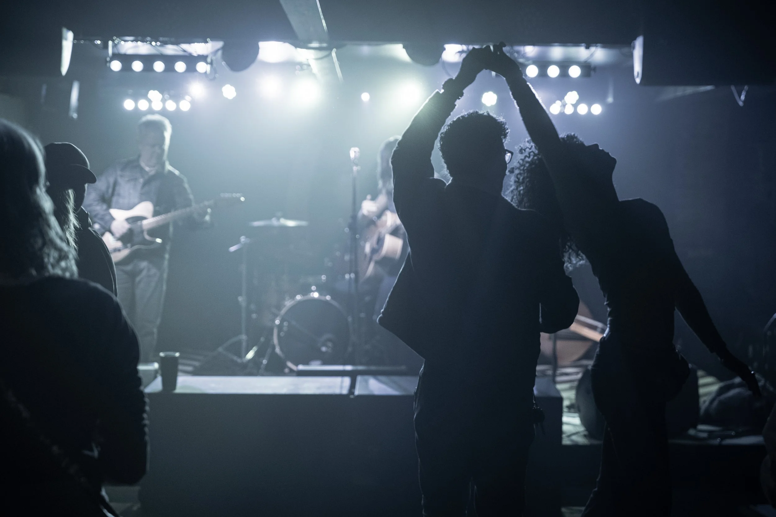 Silhouettes of a couple dancing in front of a live band on stage with bright spotlights.