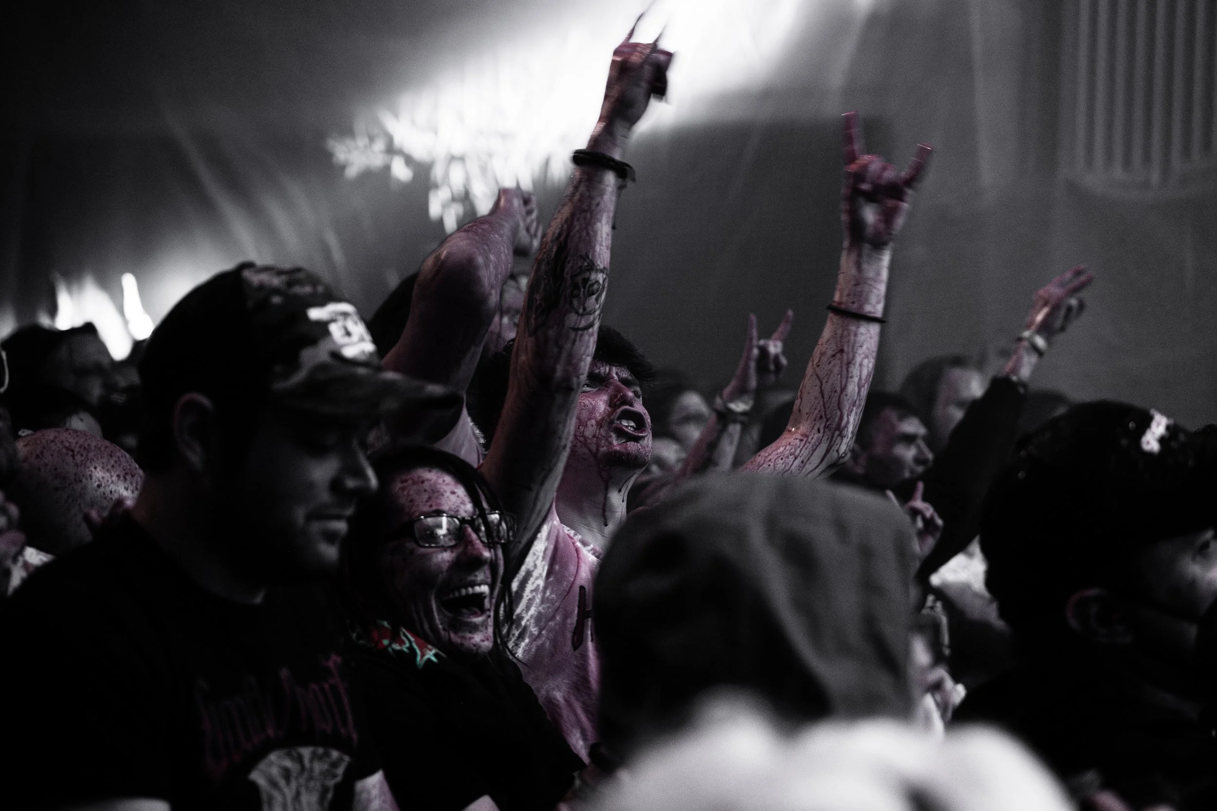 Crowd of people at a concert showing intense emotions, some with arms raised, some with bloody faces and hands, in a dark setting with stage lighting.