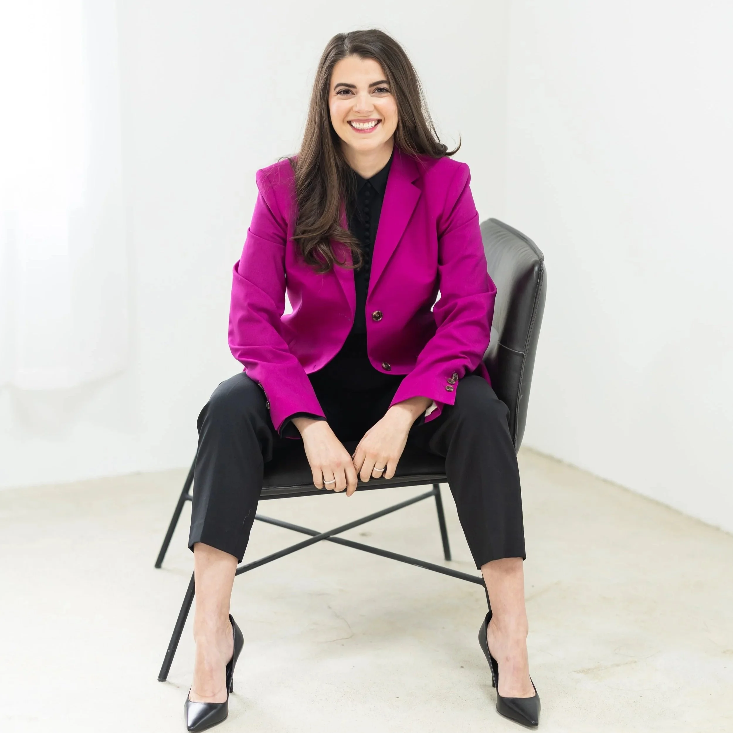 Julie Starr, certified career pivot coach, seated in a black chair wearing a magenta blazer, smiling in a bright studio setting