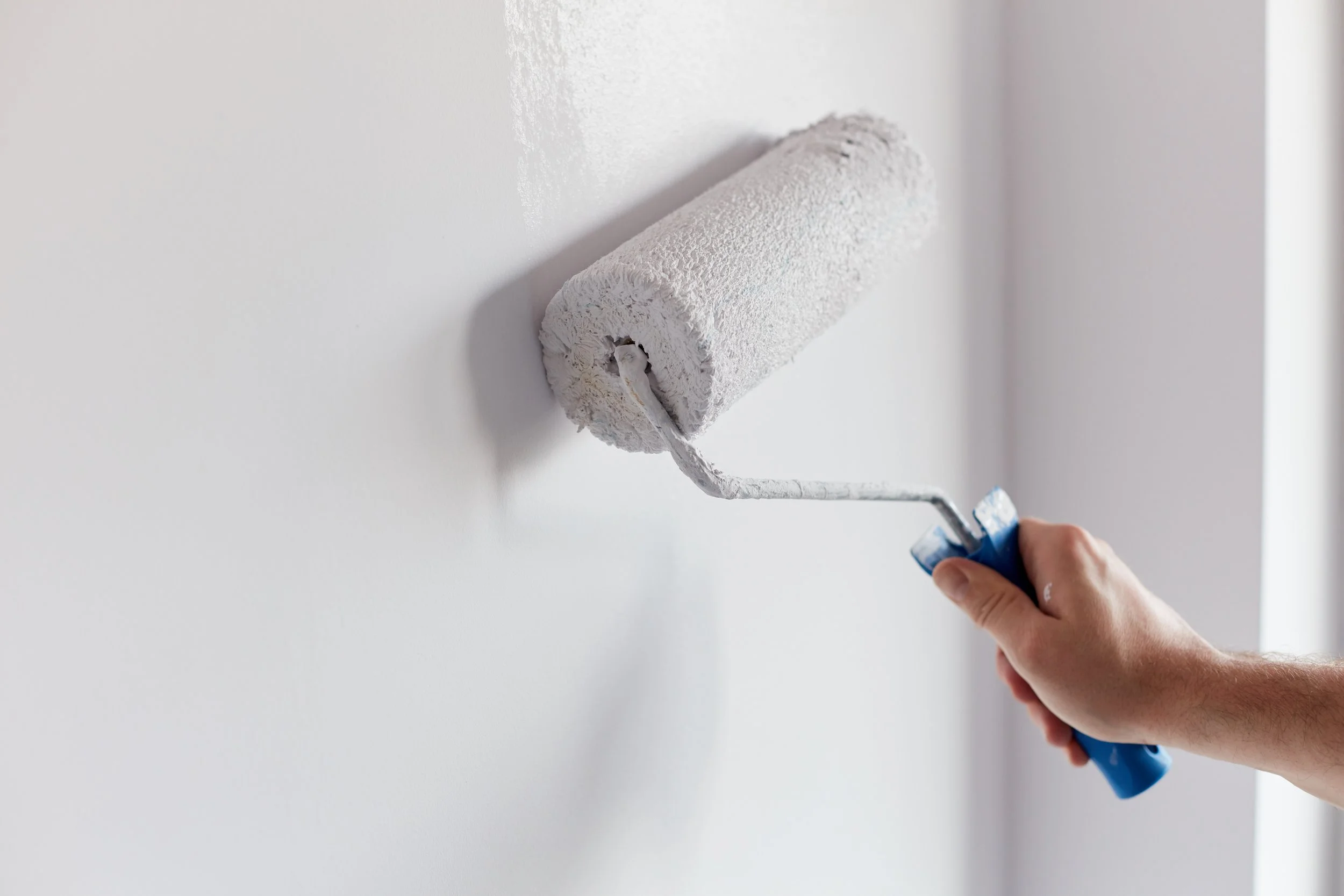 Person painting white wall with a paint roller.