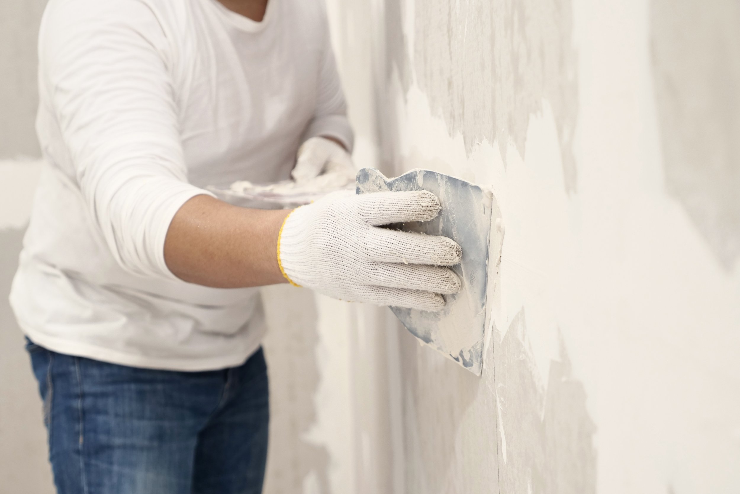 Person wearing white gloves and a white shirt smoothing drywall on a wall.
