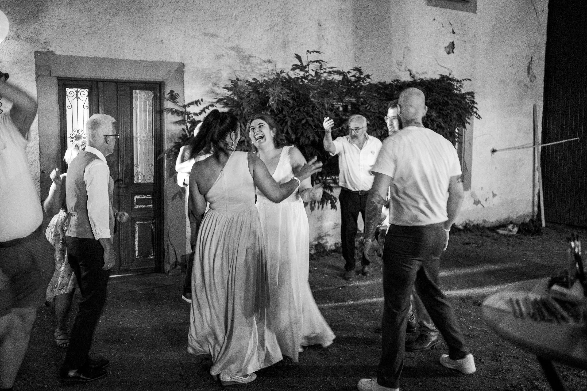 Menschen tanzen und lachen bei einer Party im Freien, am Abend, in schwarz-weiß aufgenommen.