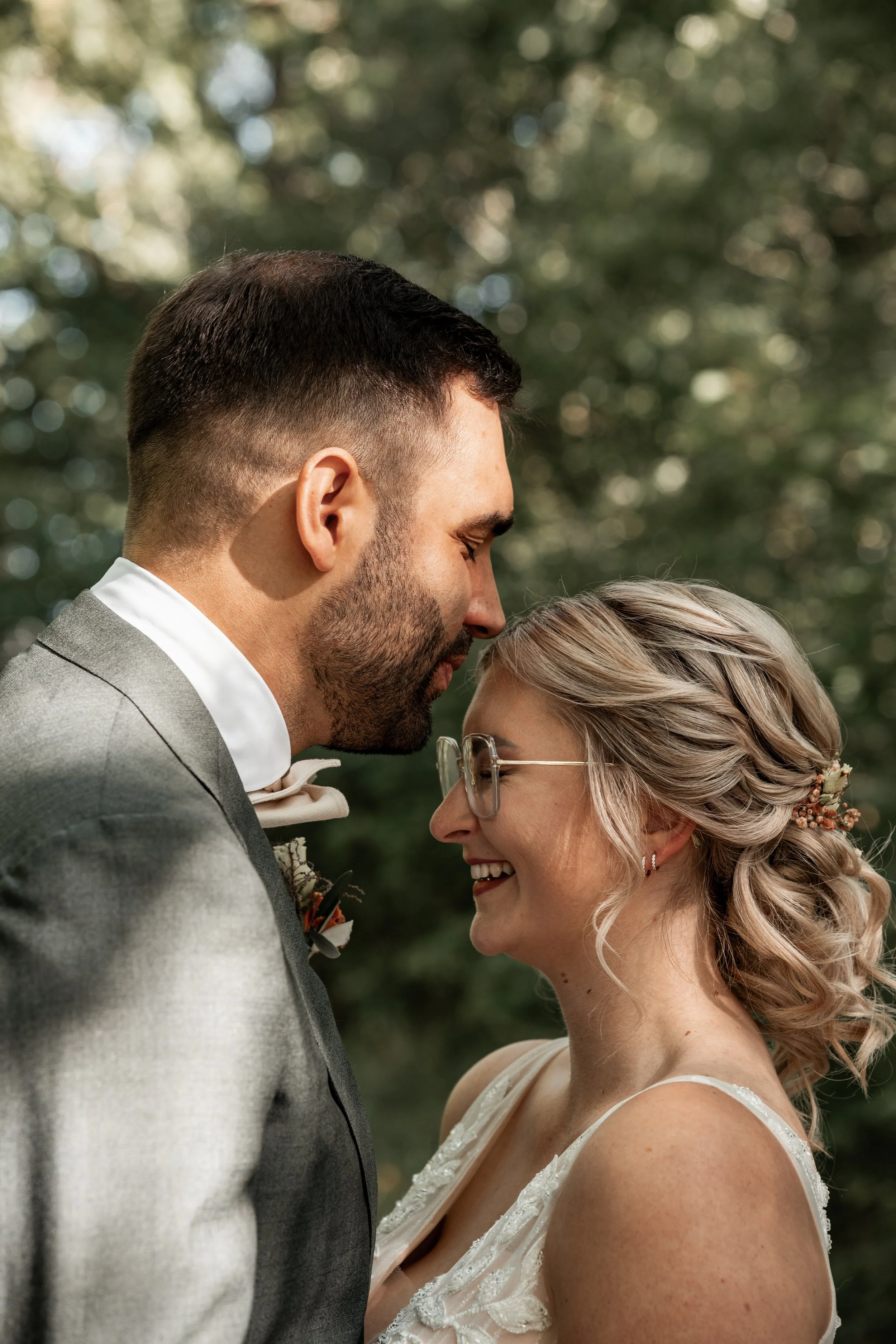 Ein Mann und eine Frau bei einer Hochzeitszeremonie stehen sich mit ihren Köpfen nahe und lächeln.